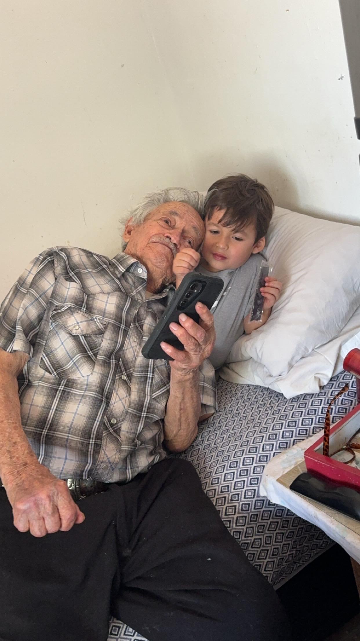 An elderly man and a young boy sit close, enjoying time together with a smartphone.