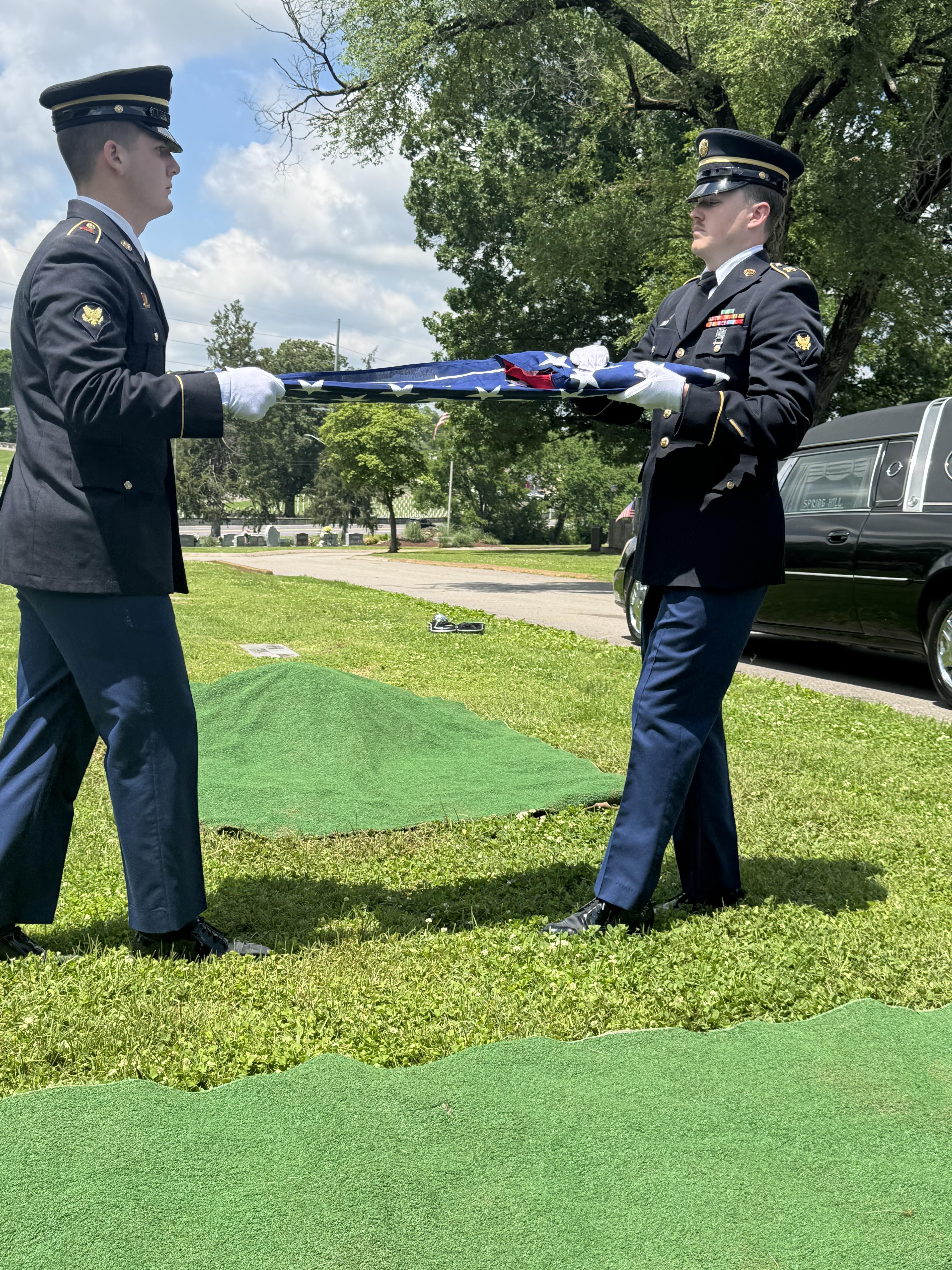 Two soldiers carefully fold a flag in a park while honoring a fallen hero during the ceremony.