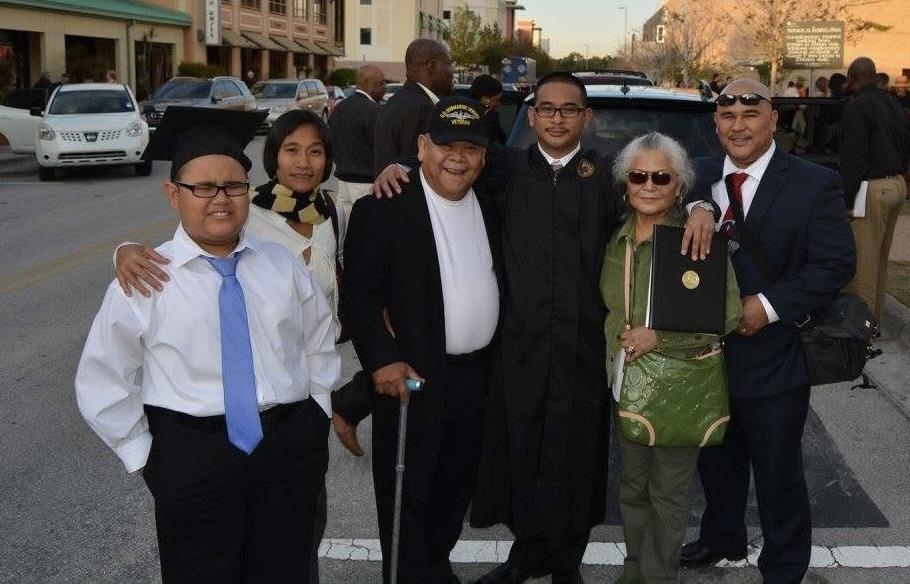 A happy family in formal attire gathers outside to celebrate a graduation.