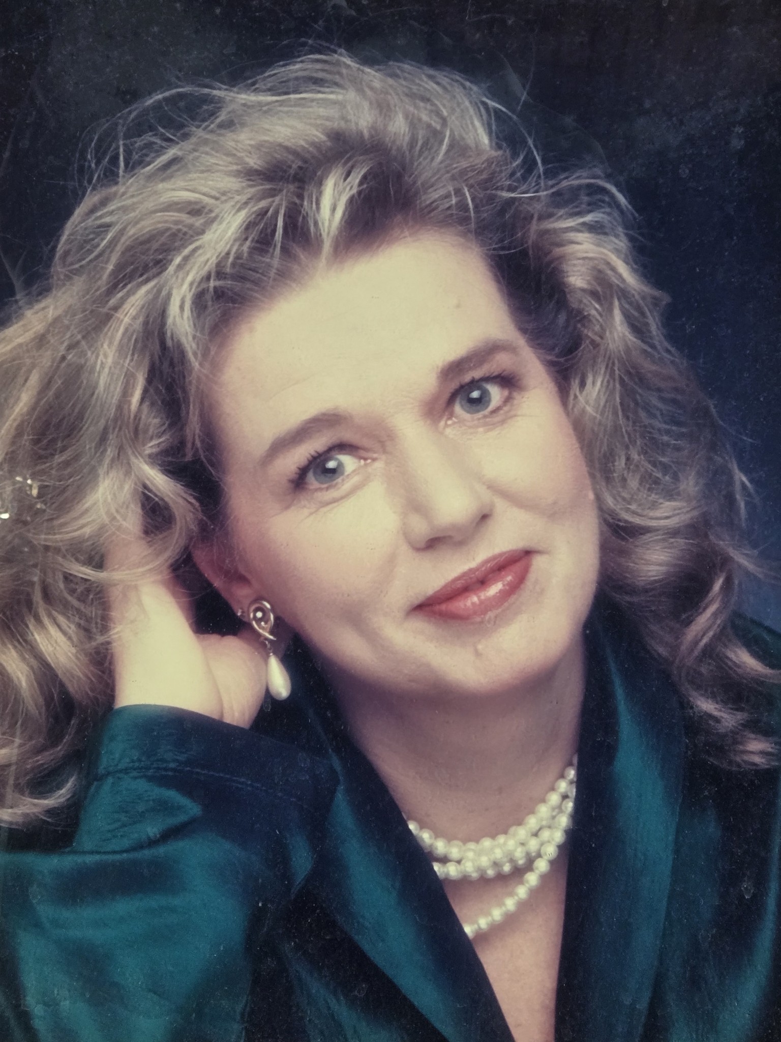 A woman with curly hair wearing a pearl necklace and a blue jacket