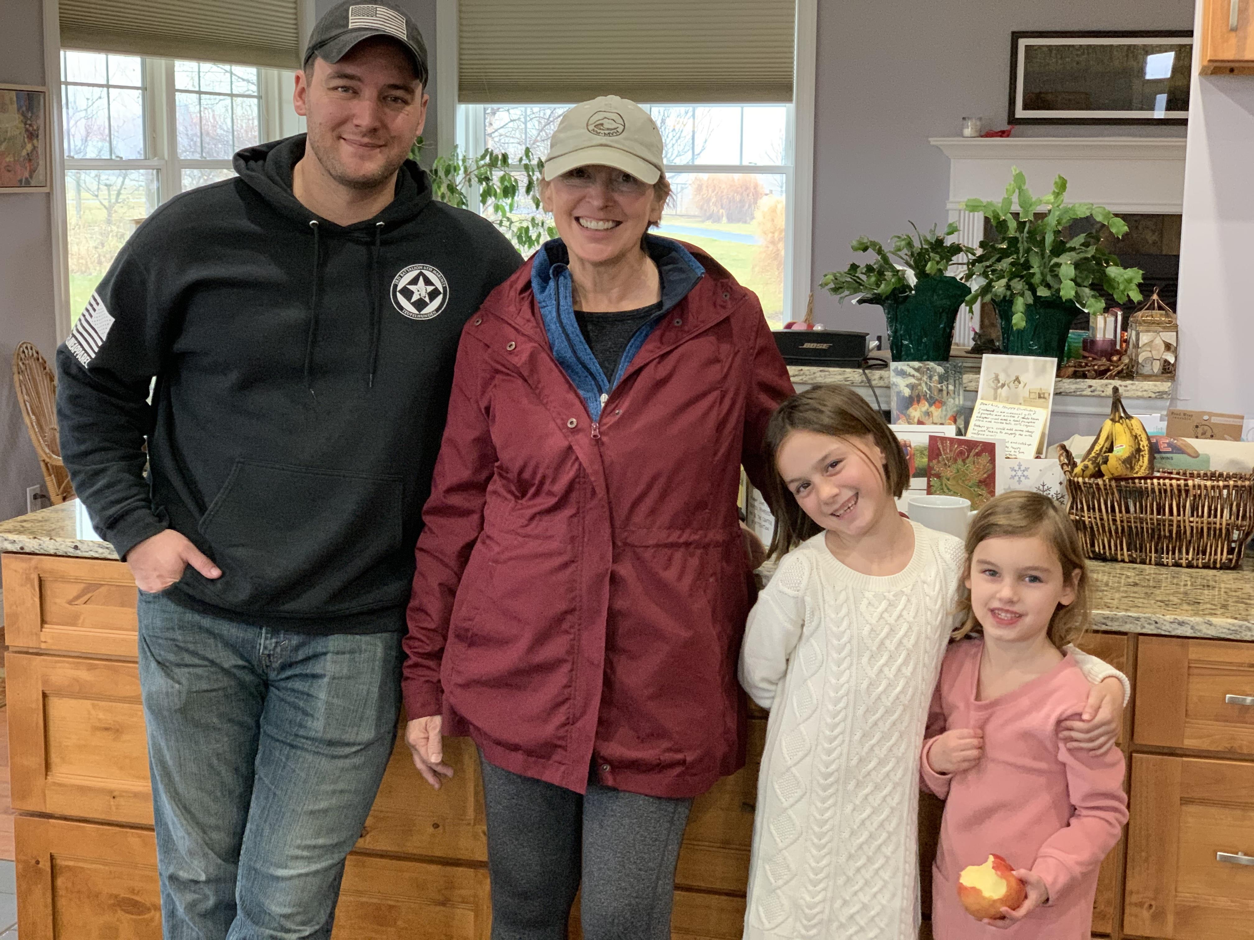 Four family members smile together in a warm kitchen filled with natural light, sharing joy.