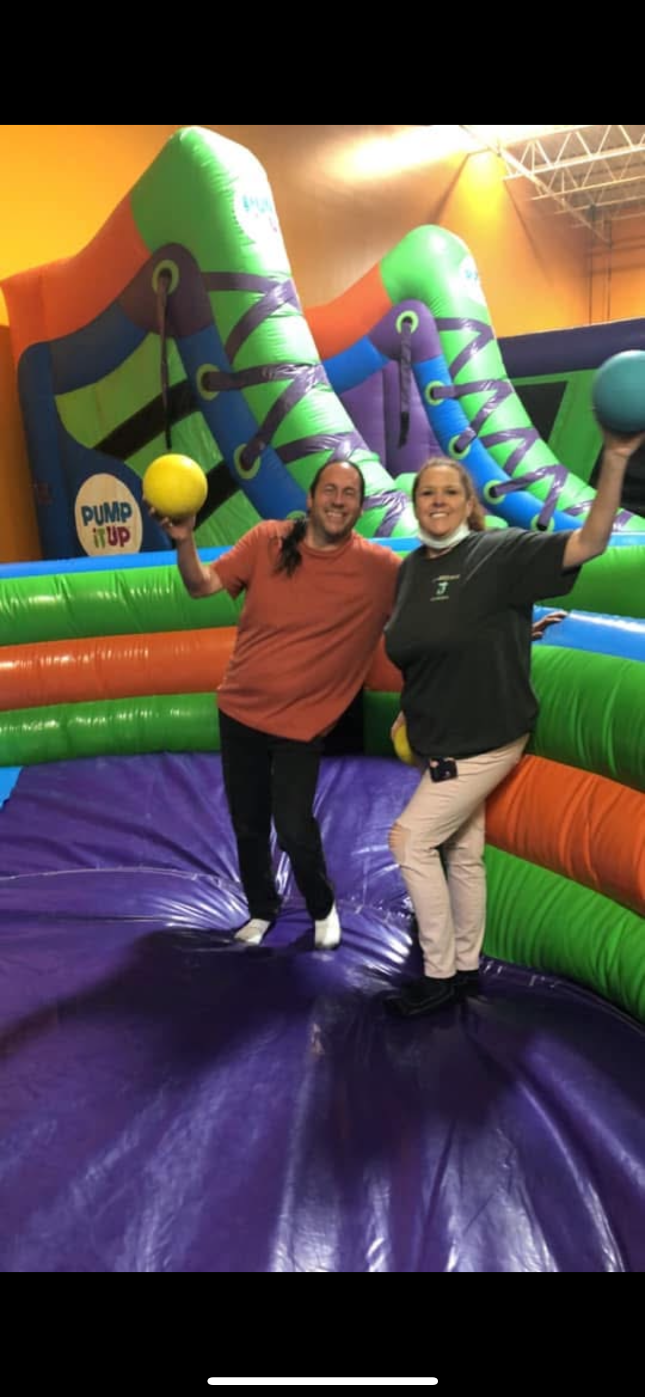 Two friends smile and pose with balls in a vibrant bounce house during indoor playtime.