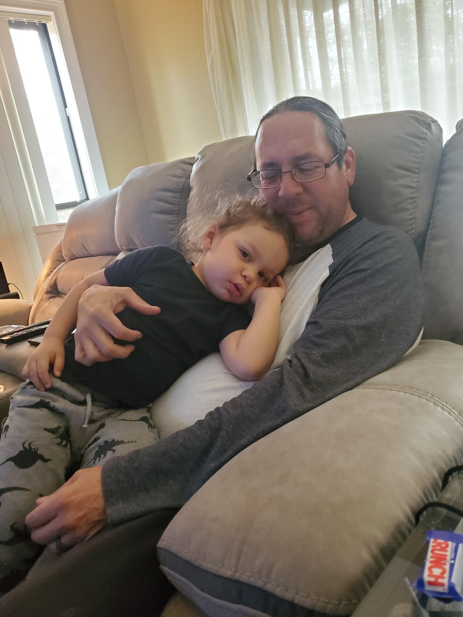 A father holds his child comfortably while sitting on a couch, enjoying a peaceful moment together.
