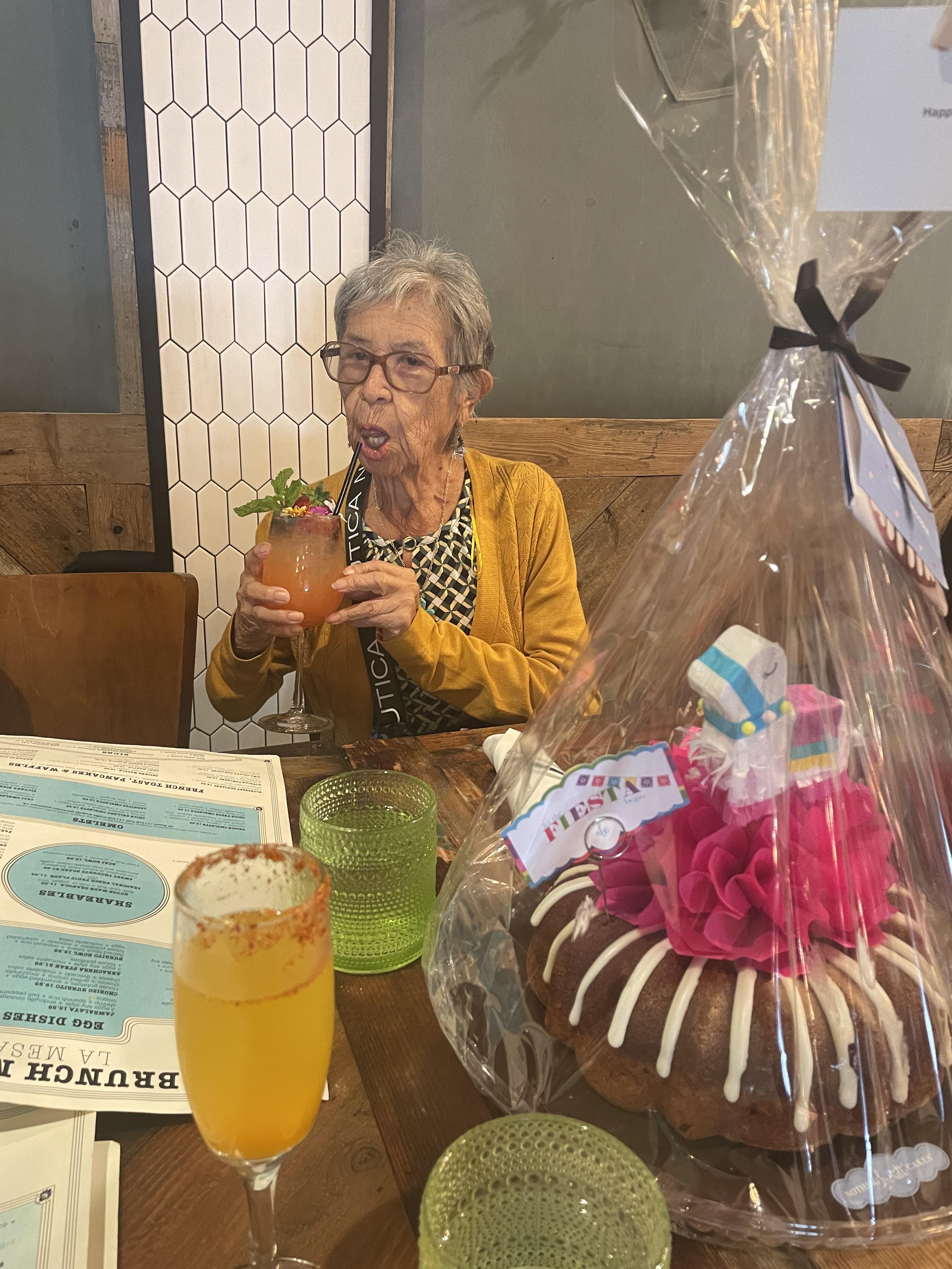 An elderly woman savoring a vibrant drink while celebrating with friends at a restaurant.