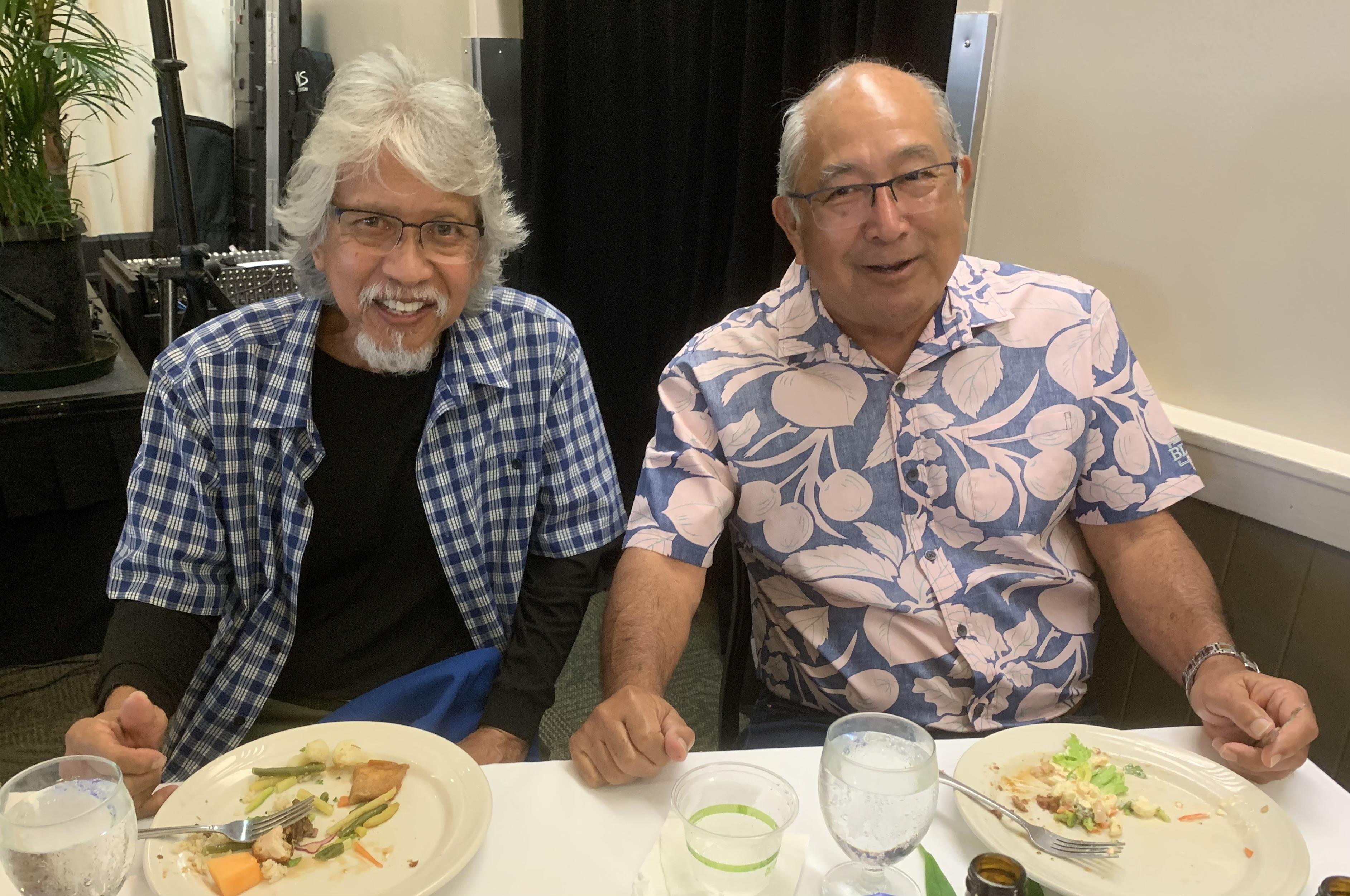 Two men are seated at a dining table, sharing a pleasant conversation while enjoying their meals.