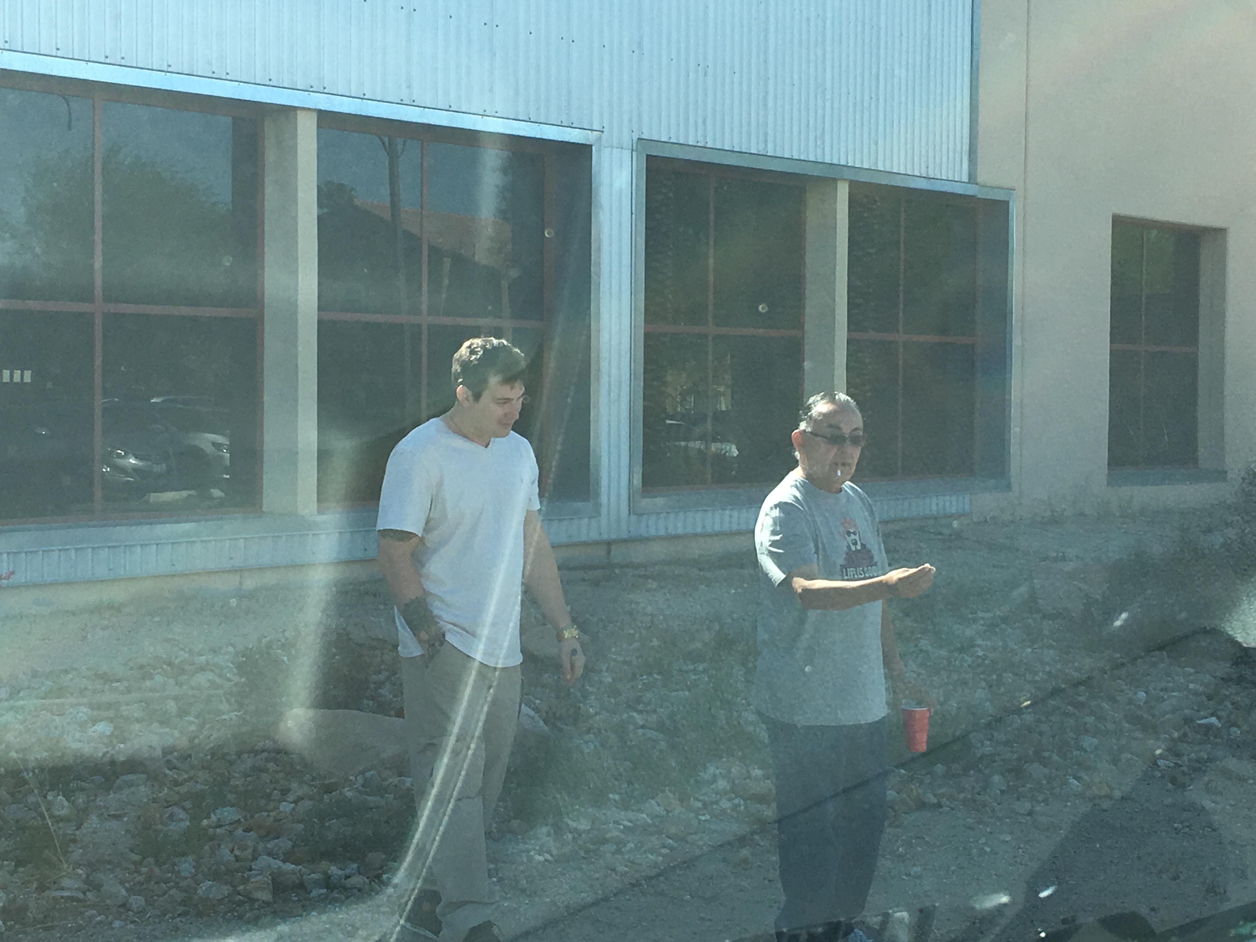 Two men are walking beside a building with construction work. It is sunny outside.
