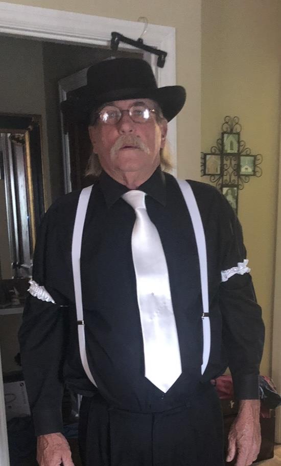 An older man in a black shirt and suspenders confidently poses in a hallway.