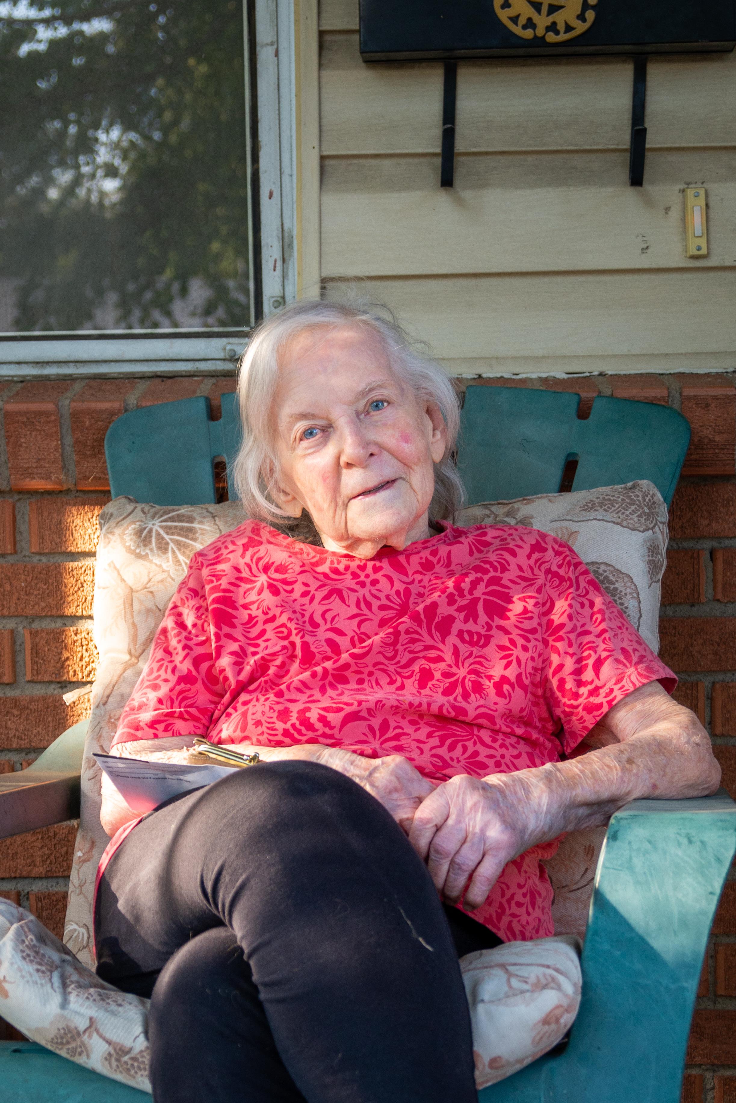 Elderly woman in a pink shirt relaxes on the porch, enjoying the warm afternoon sun.