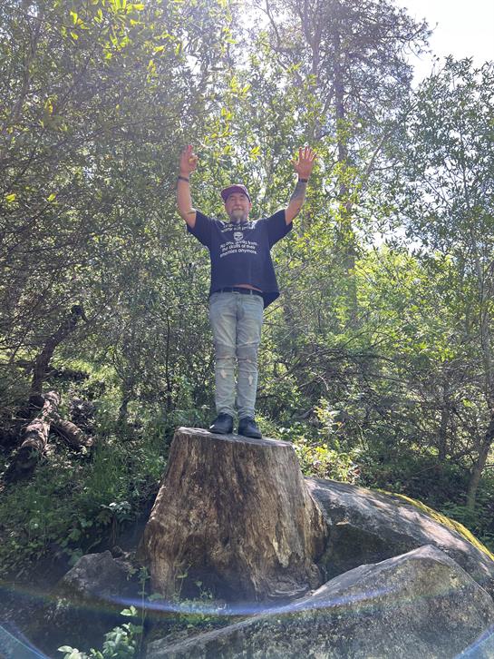 A man standing on a tree stump with his hands up