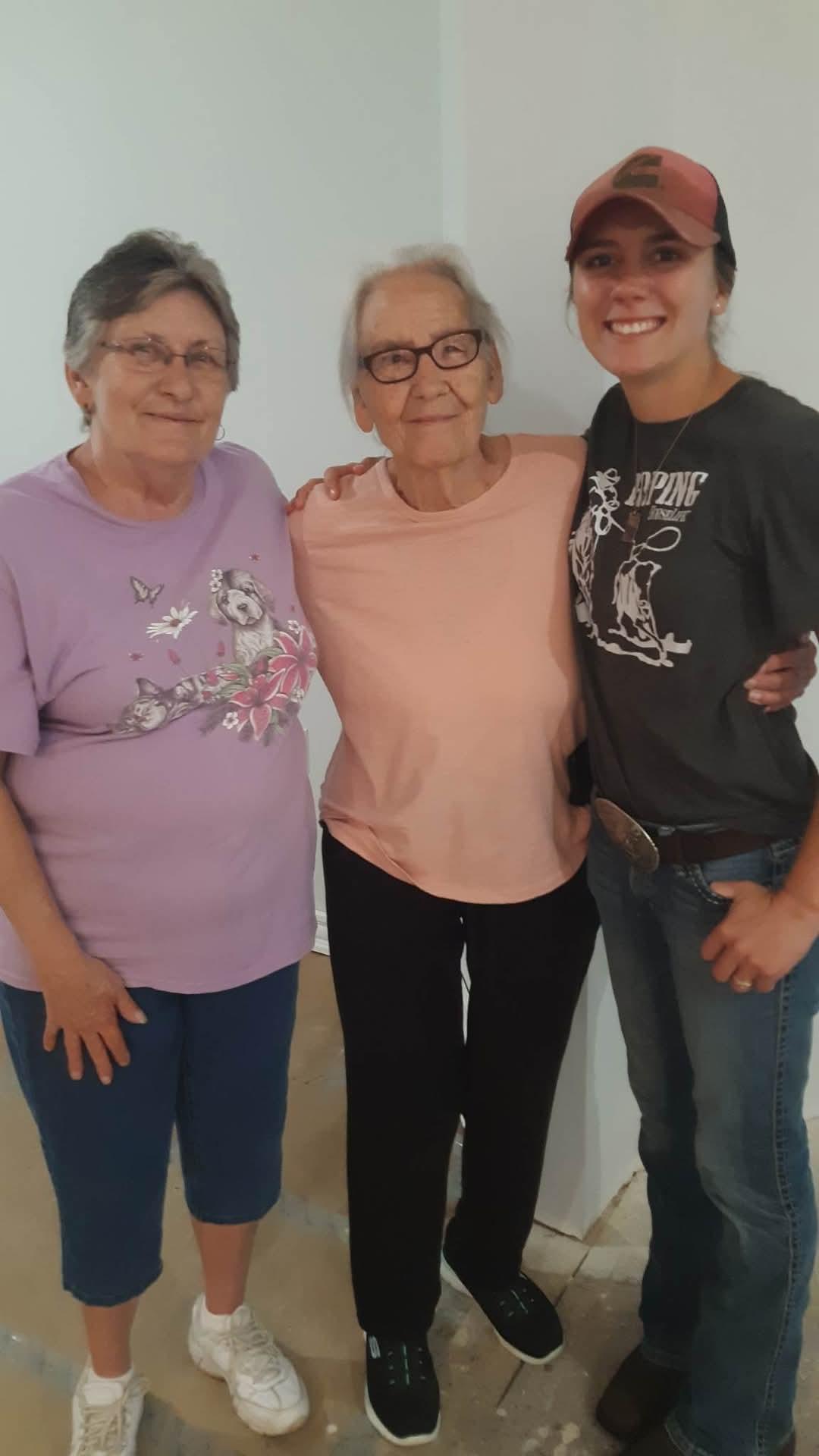 Three women pose happily indoors, showcasing their strong bond and joy in the moment.