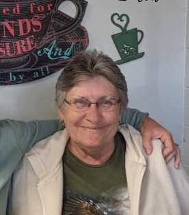 Elderly woman smiles with joy while standing beside a friend at a casual coffee shop.