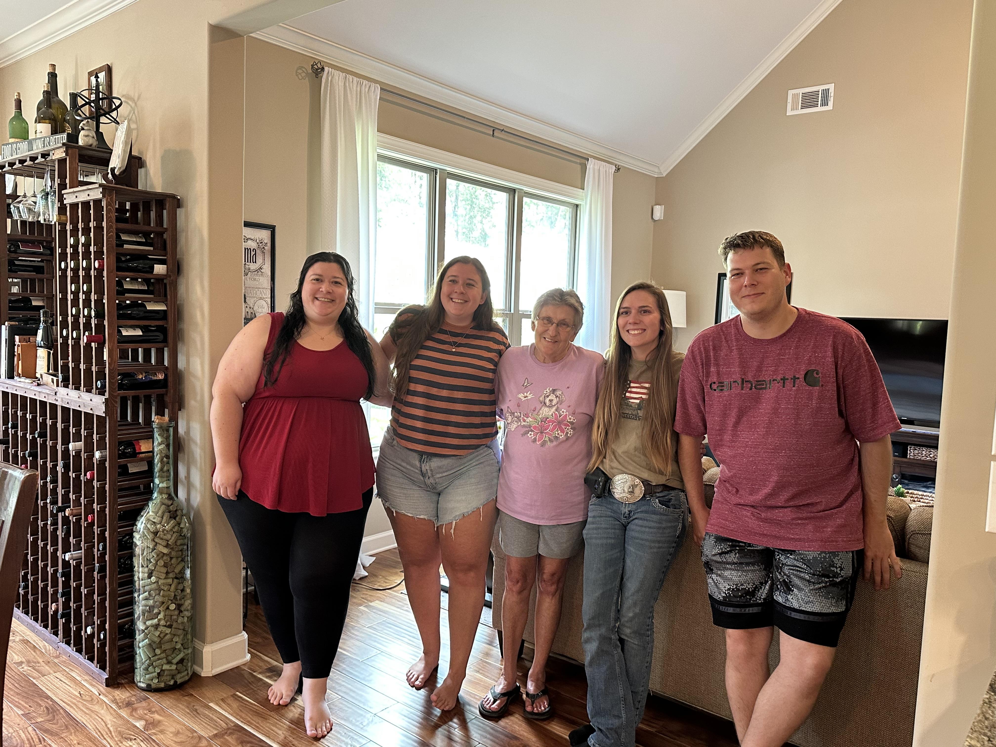 A group of five family members poses happily in a welcoming living room, enjoying their time.