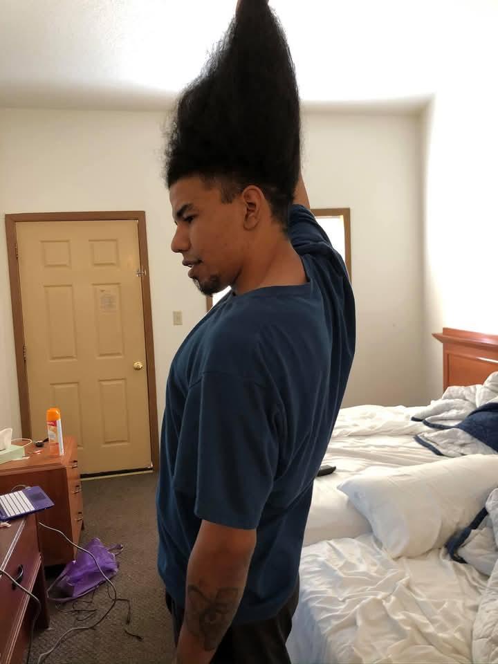 A person showcases an impressive tall hairstyle in a casual bedroom setting, relaxed morning vibes.