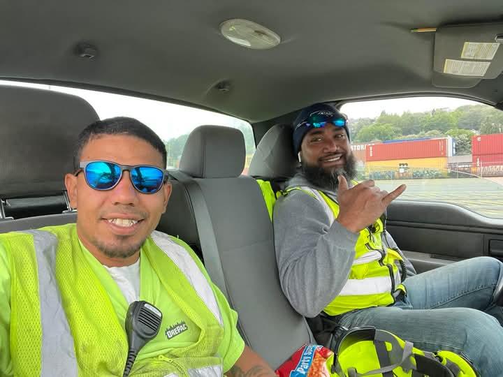Two workers enjoy a break inside a truck while surrounded by cargo containers at a port.