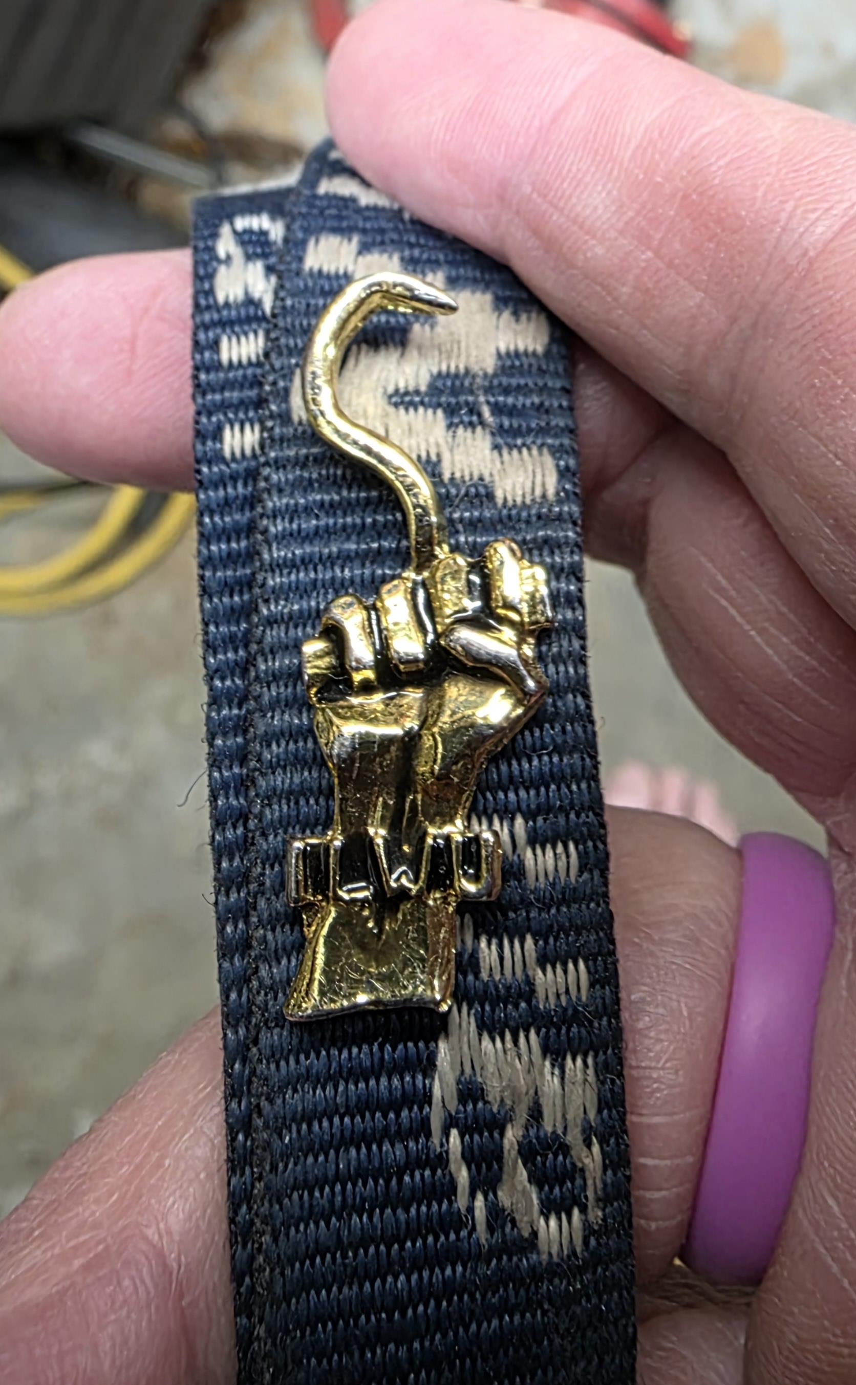A hand is holding a fabric strap featuring a bold gold fist emblem in a relaxed indoor space.