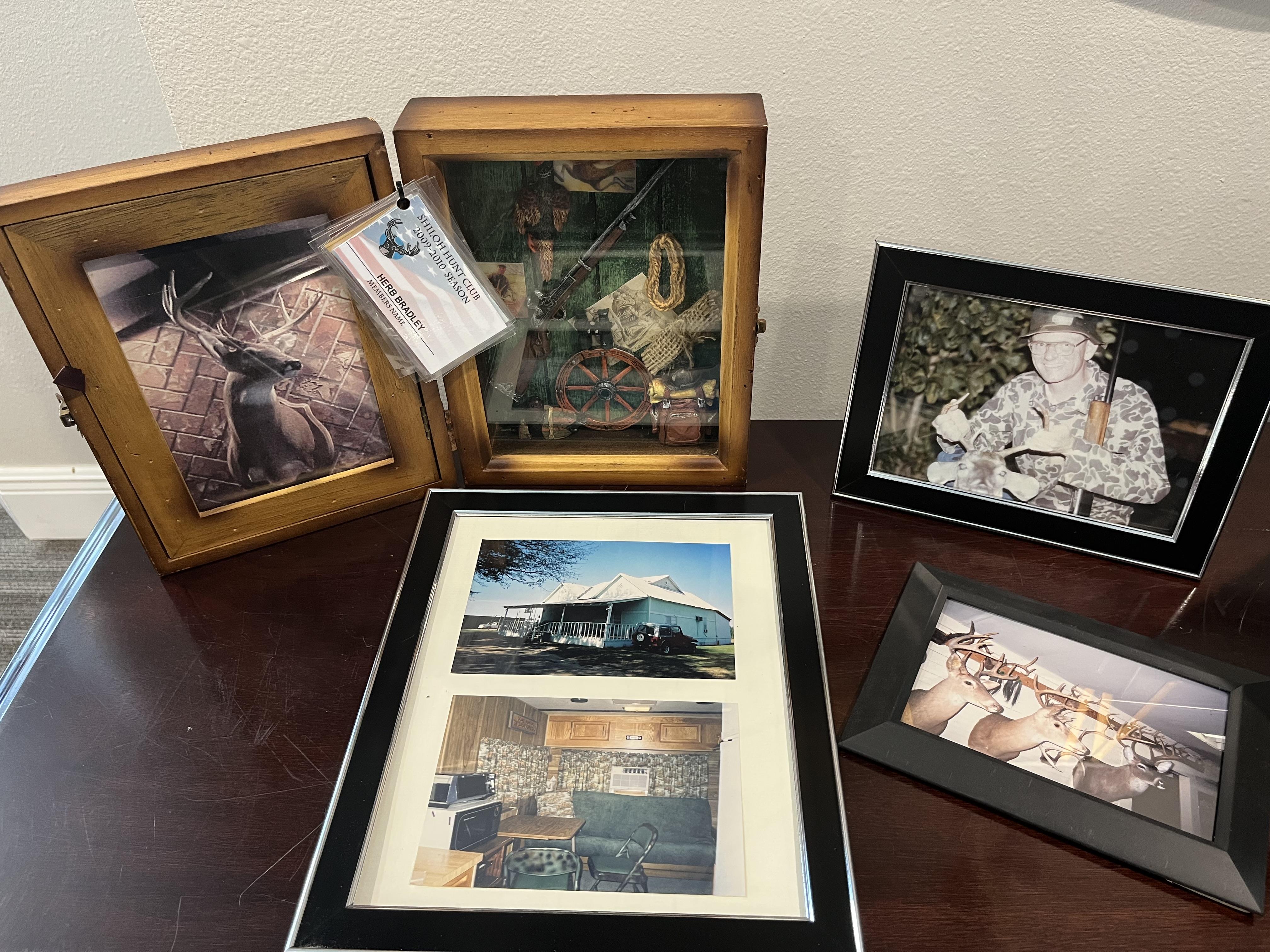 Display of framed photographs depicting hunting trophies and outdoor landscapes on a desk.
