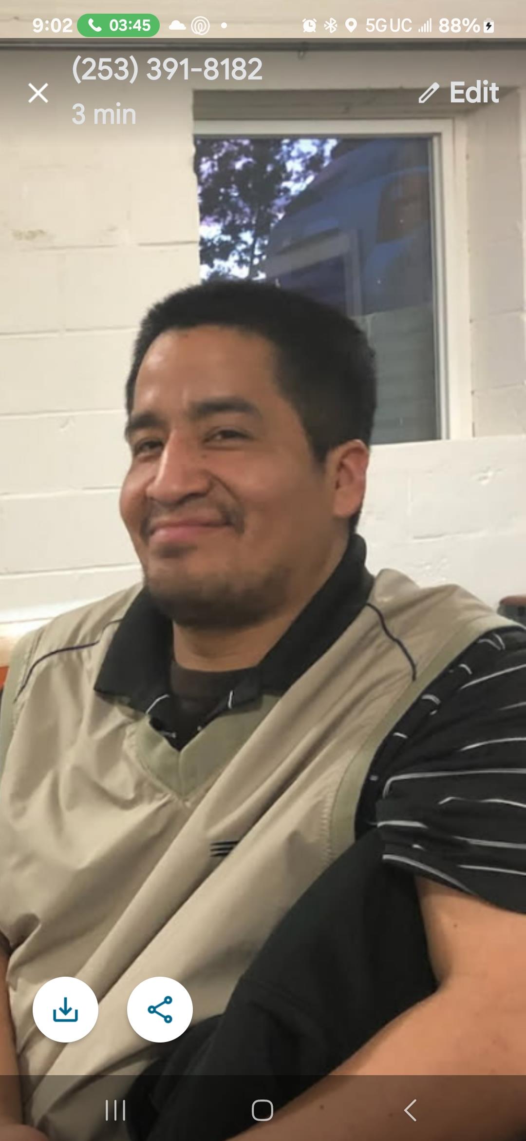 A man with a friendly smile sits comfortably indoors, enjoying a relaxed moment with friends.