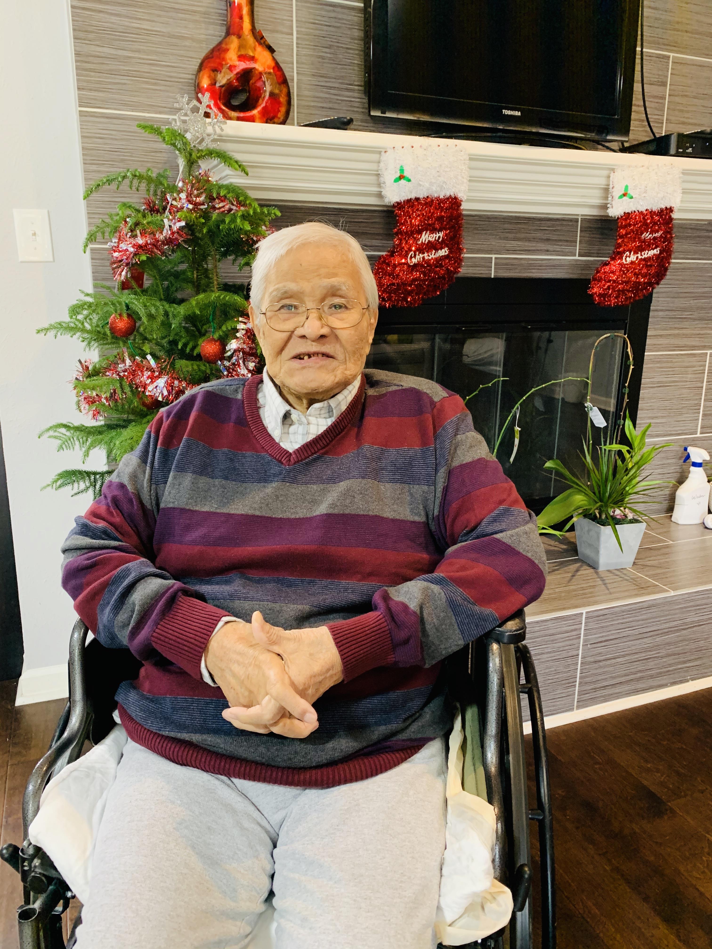 An elderly man enjoys the holiday spirit while sitting comfortably near a Christmas tree.
