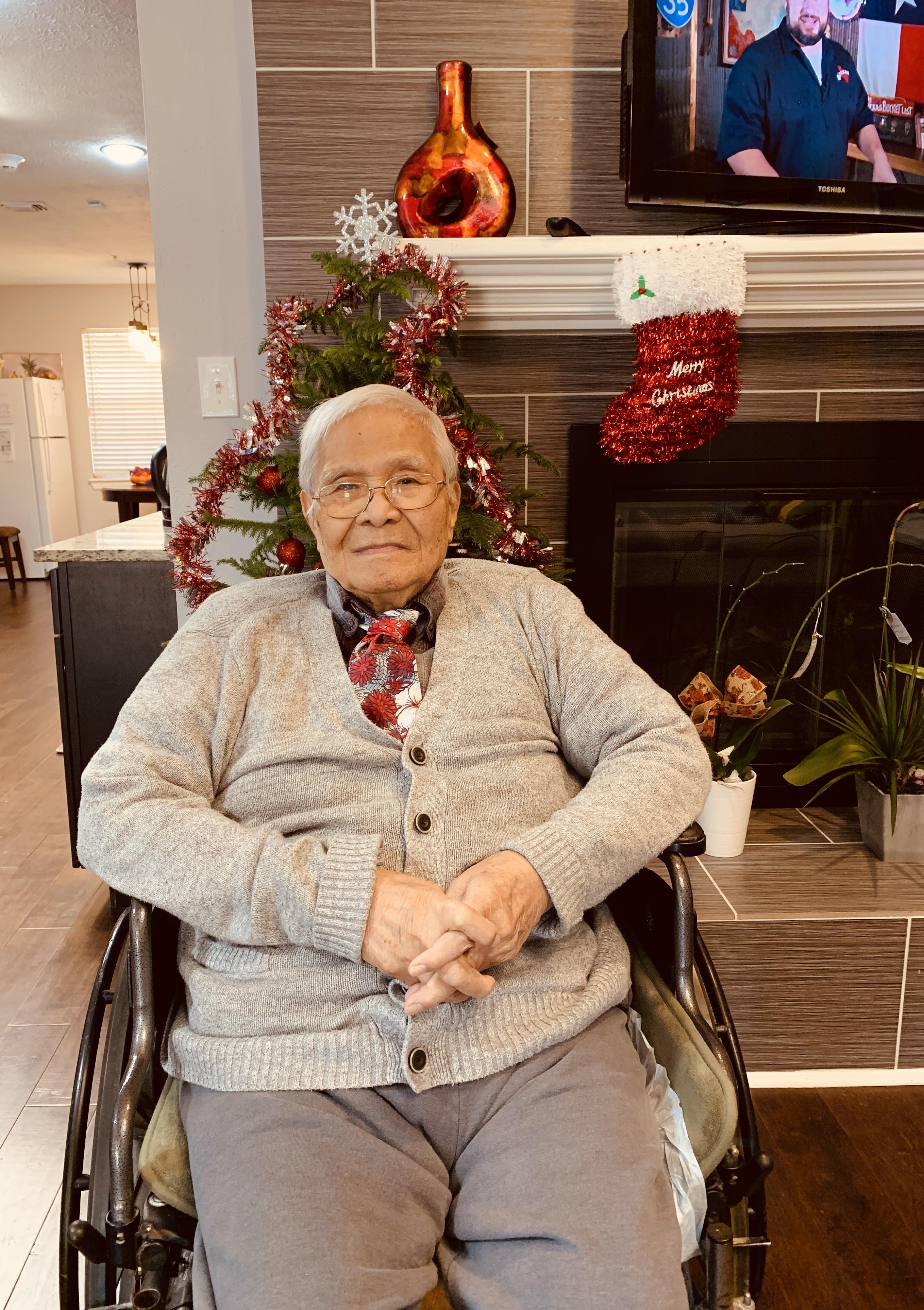 An elderly man relaxes in a wheelchair amid festive Christmas decor in a cozy living room.