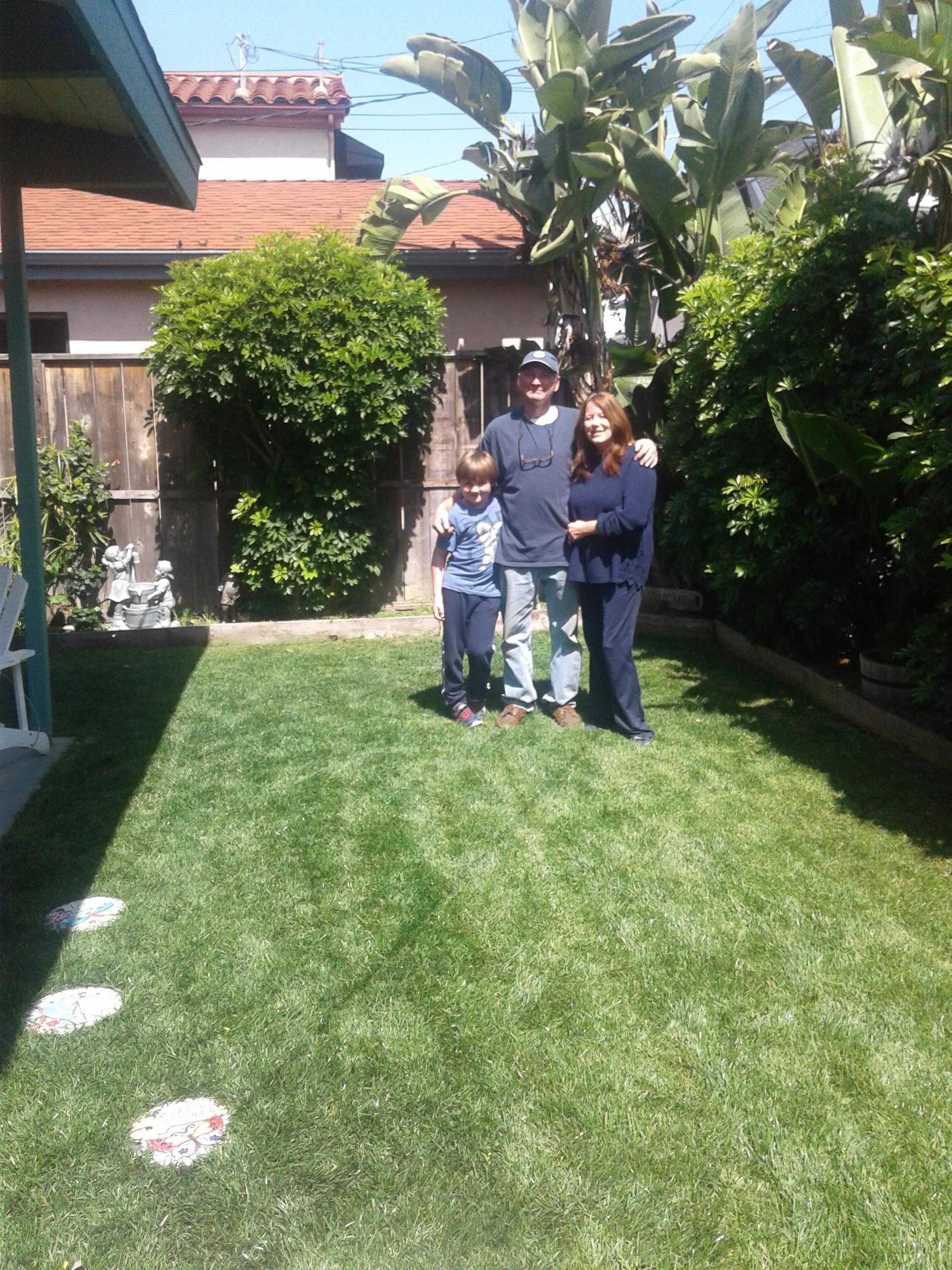 Happy family poses together in their backyard, enjoying a bright sunny day surrounded by plants.