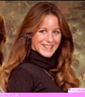 Woman with long, flowing hair smiles at the camera, wearing a black turtleneck in a vintage setting.