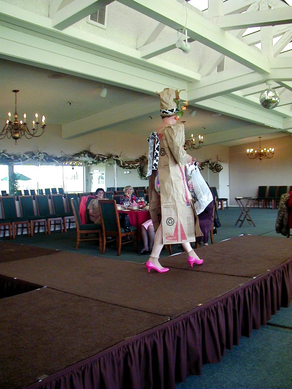 A model walks the runway in a creative outfit made from recycled materials at an event.