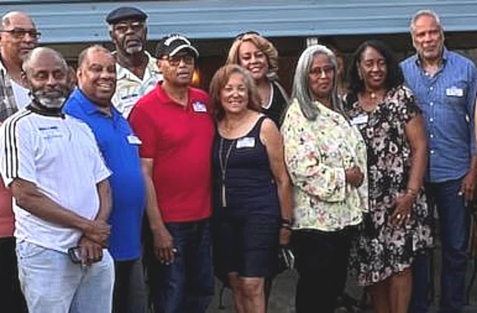 Friends celebrate a reunion outside a venue on a sunny summer afternoon.