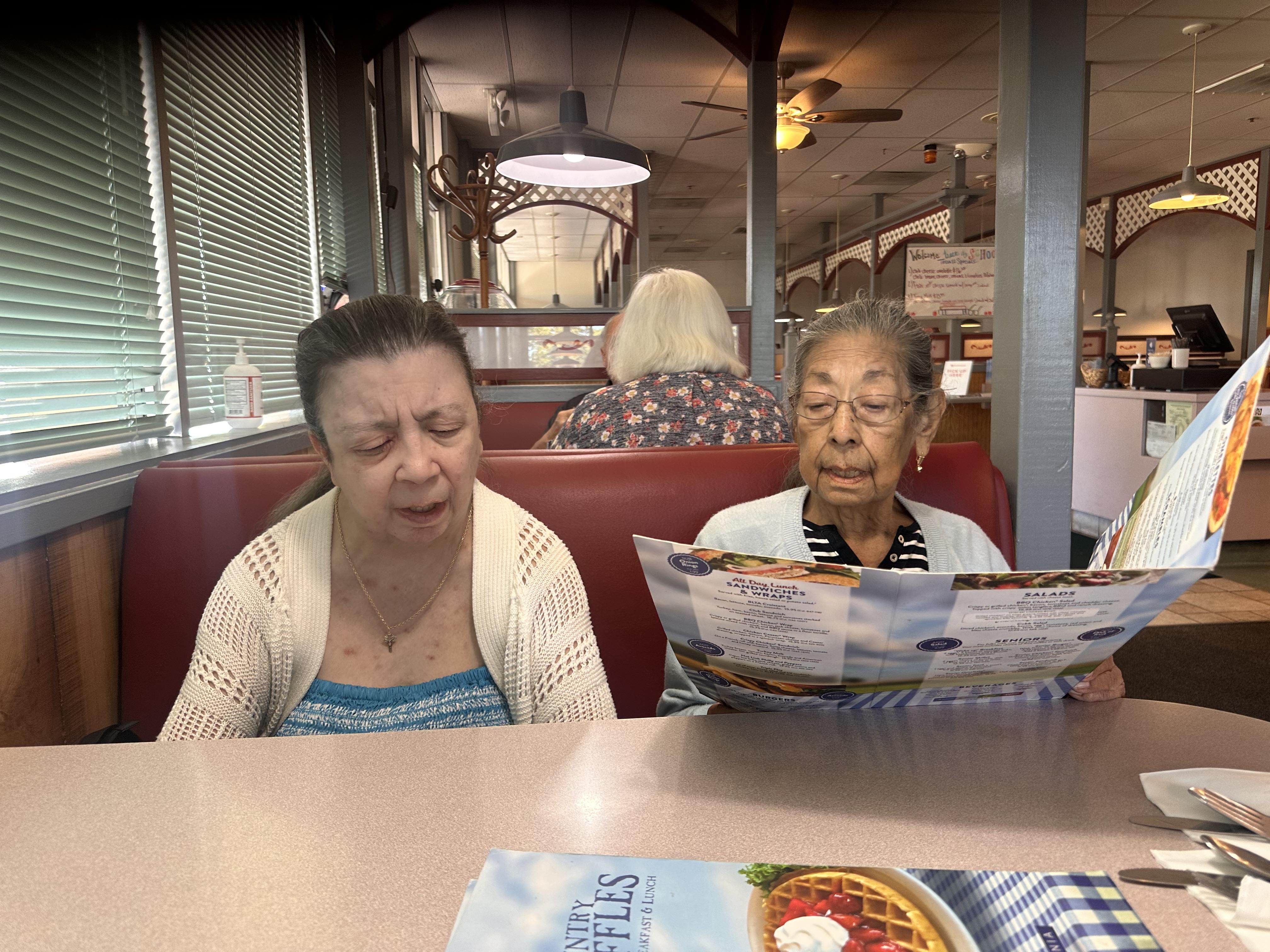 Two elderly women are seated at a booth, reviewing the menu in a diner while sharing a moment.