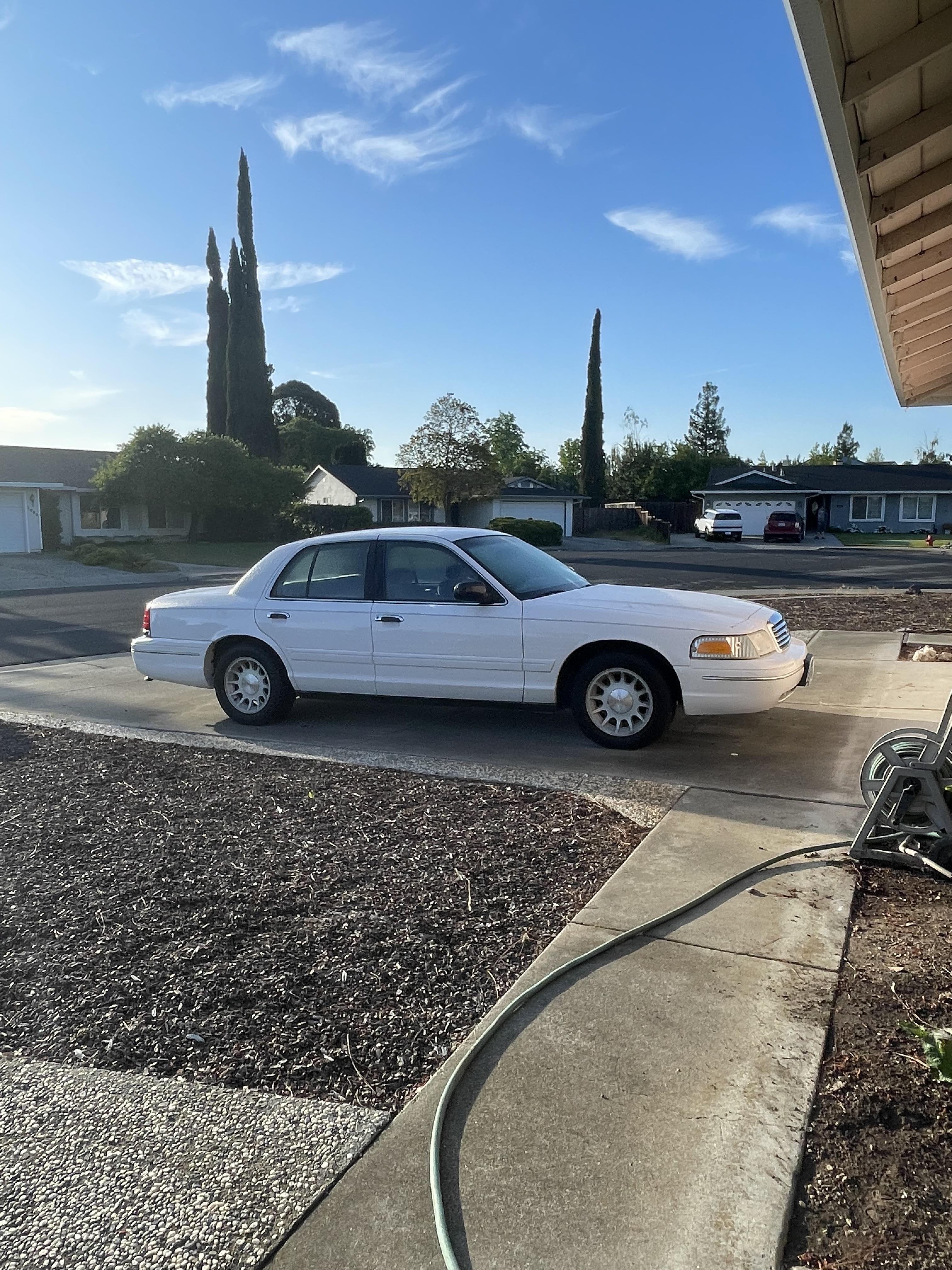 A white sedan is parked on a concrete driveway next to a house with clear skies above.