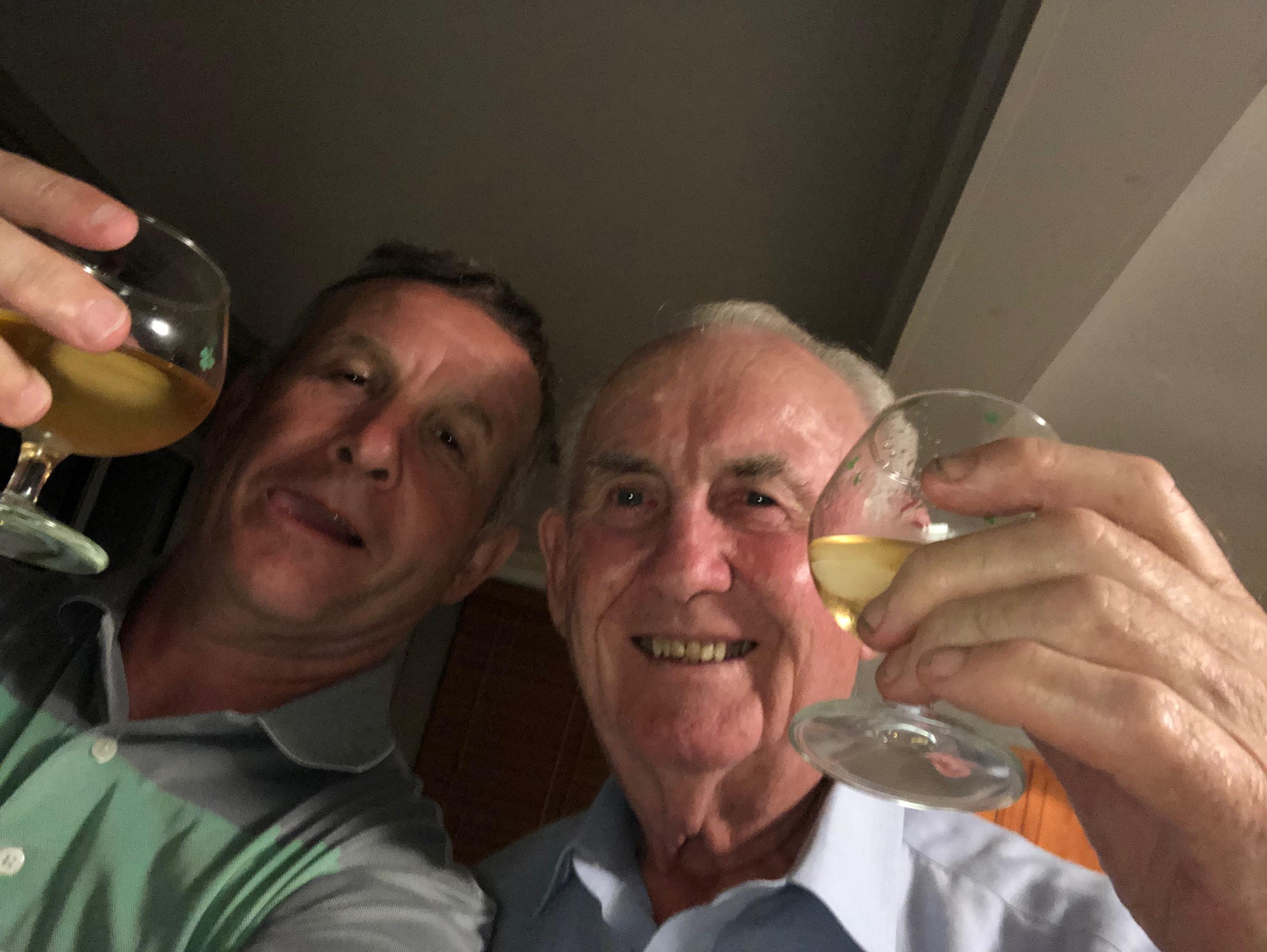 Two men are smiling and raising their glasses in a cheerful toast during a celebration.
