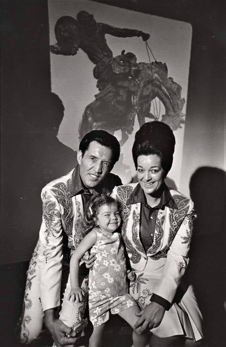 Performers dressed in classic attire sit with a smiling young girl in a beautifully lit studio.
