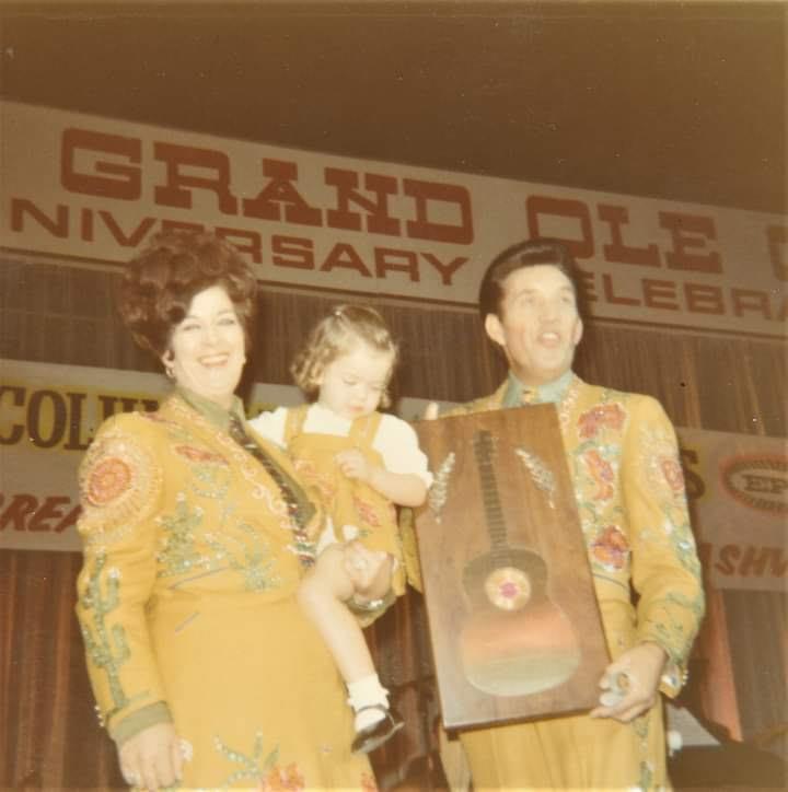 Performers celebrate at the Grand Ole Opry anniversary with a child, capturing a memorable moment.