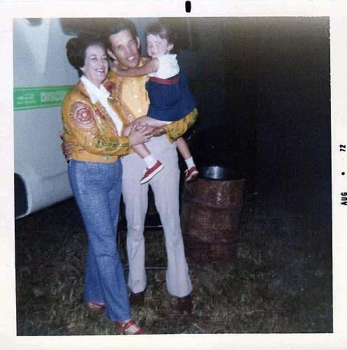 A couple proudly holds their child during a warm evening at a local festival in the 1970s.