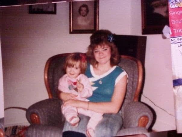 A mother sits in a patterned chair holding her smiling daughter in a warm, inviting home.