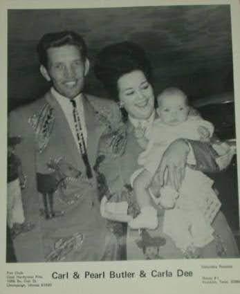 A couple holds their baby while smiling at a family gathering, showcasing warmth and togetherness.
