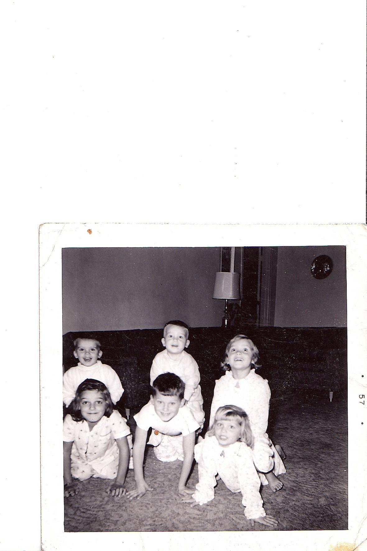 Six children are happily engaged in a playful pyramid formation on a carpeted floor.