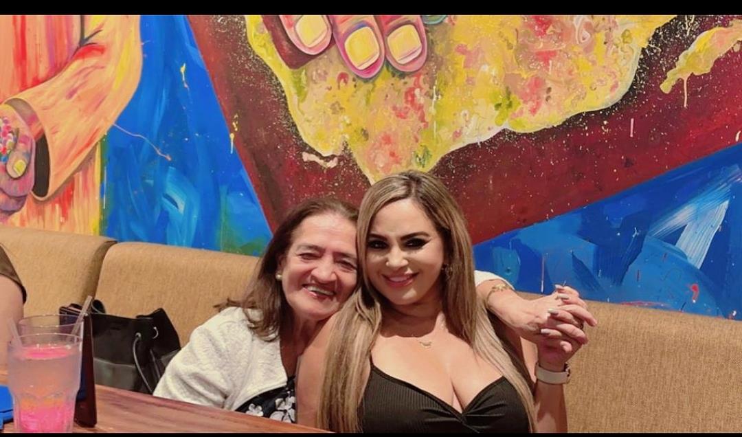 Two women embrace happily in a lively restaurant with bright murals during the evening.