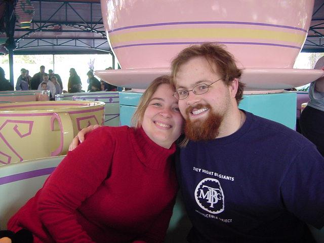 Couple smiles together on a colorful spinning ride at a lively amusement park attraction.