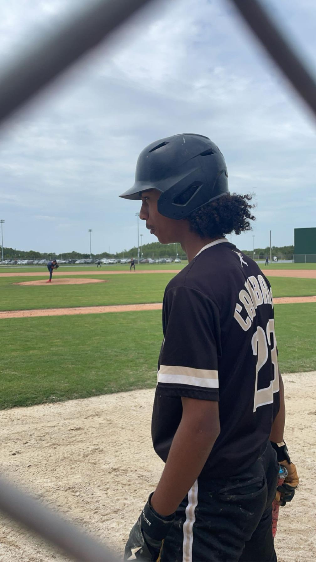 A young athlete clad in a black baseball uniform watches the game intently from the field.