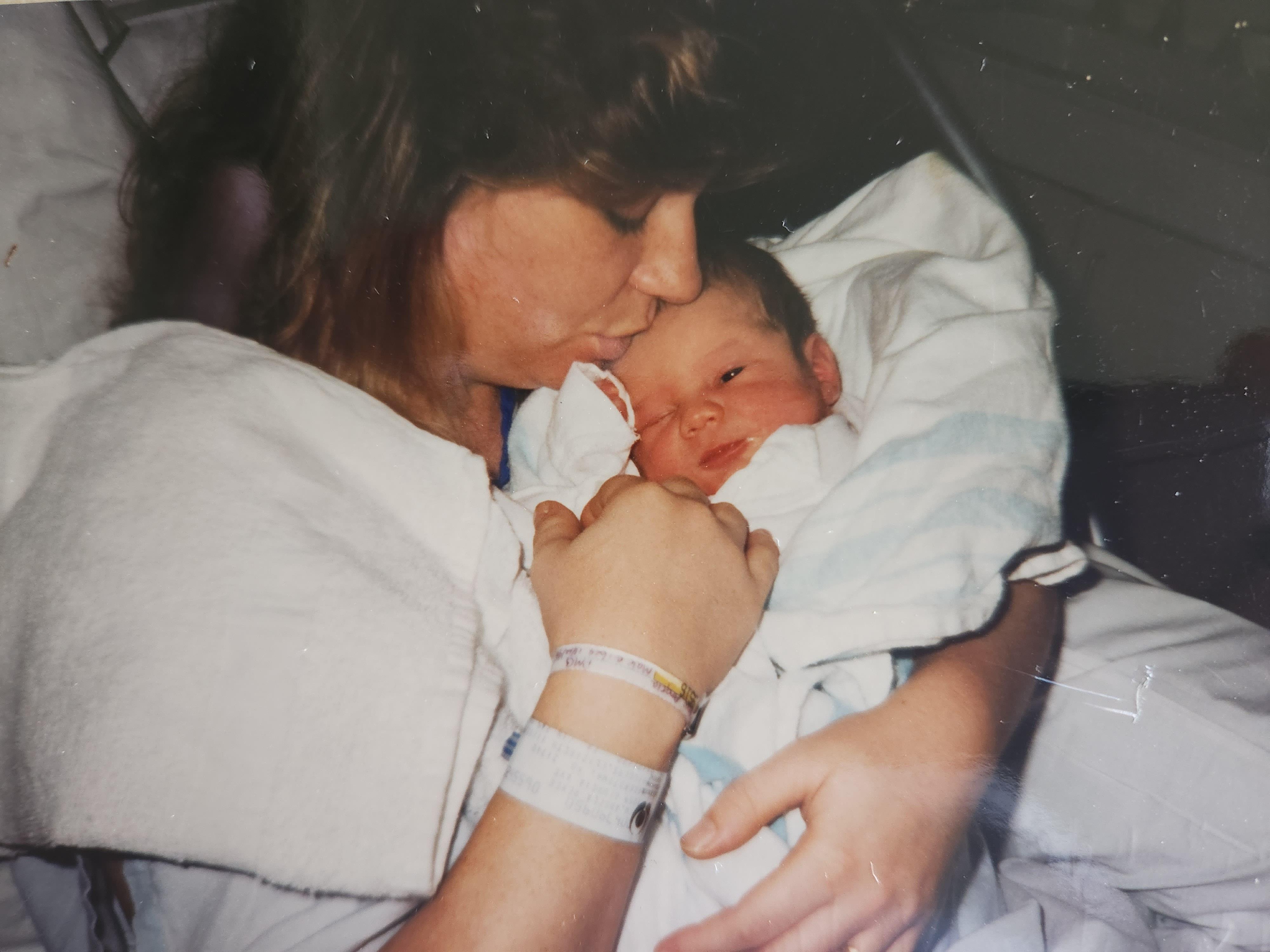 A mother kisses her newborn in the hospital, sharing a loving bond after birth.