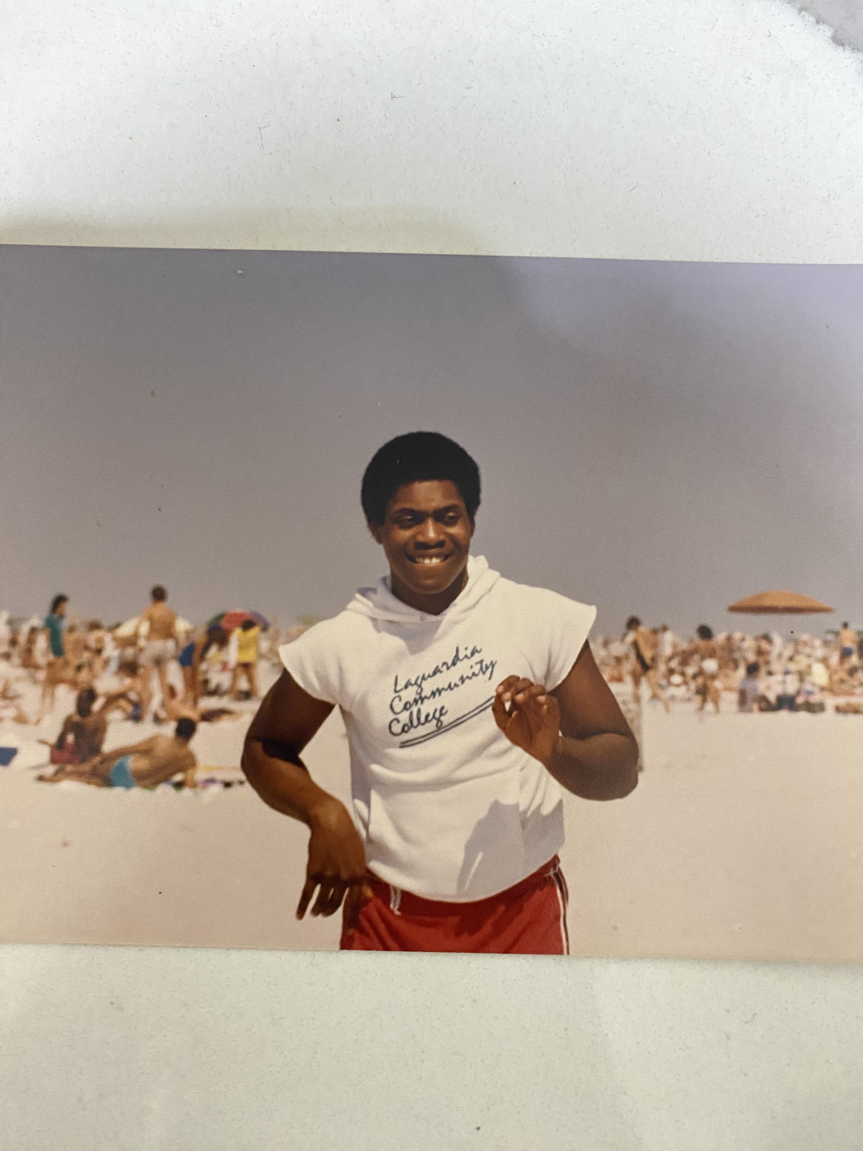 A person in a white sleeveless shirt enjoys a sunny beach day with other beachgoers.