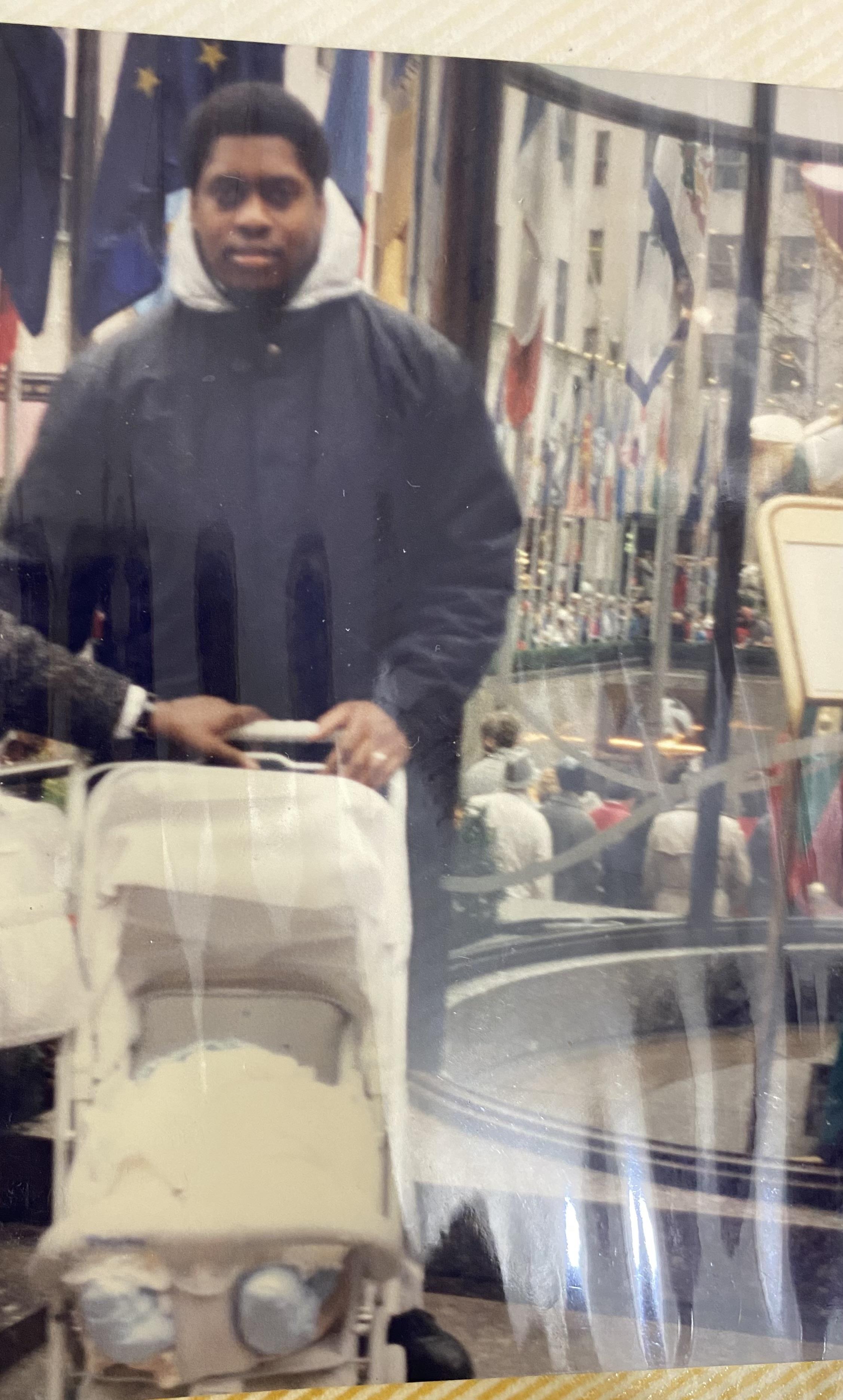A man is navigating a stroller through a bustling street filled with colorful flags and people.
