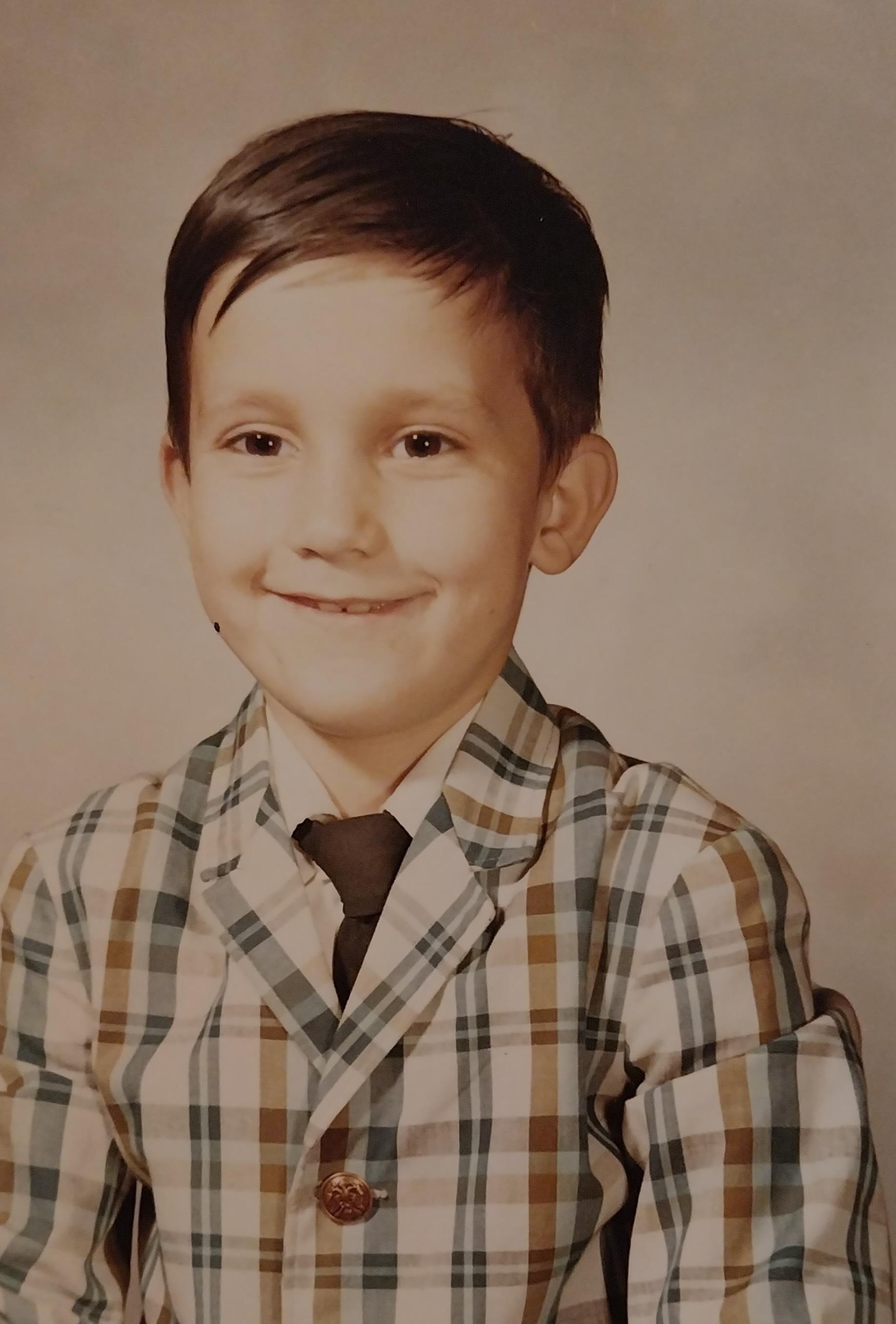 A young boy is smiling while wearing a plaid suit and a tie, showcasing a nostalgic look.