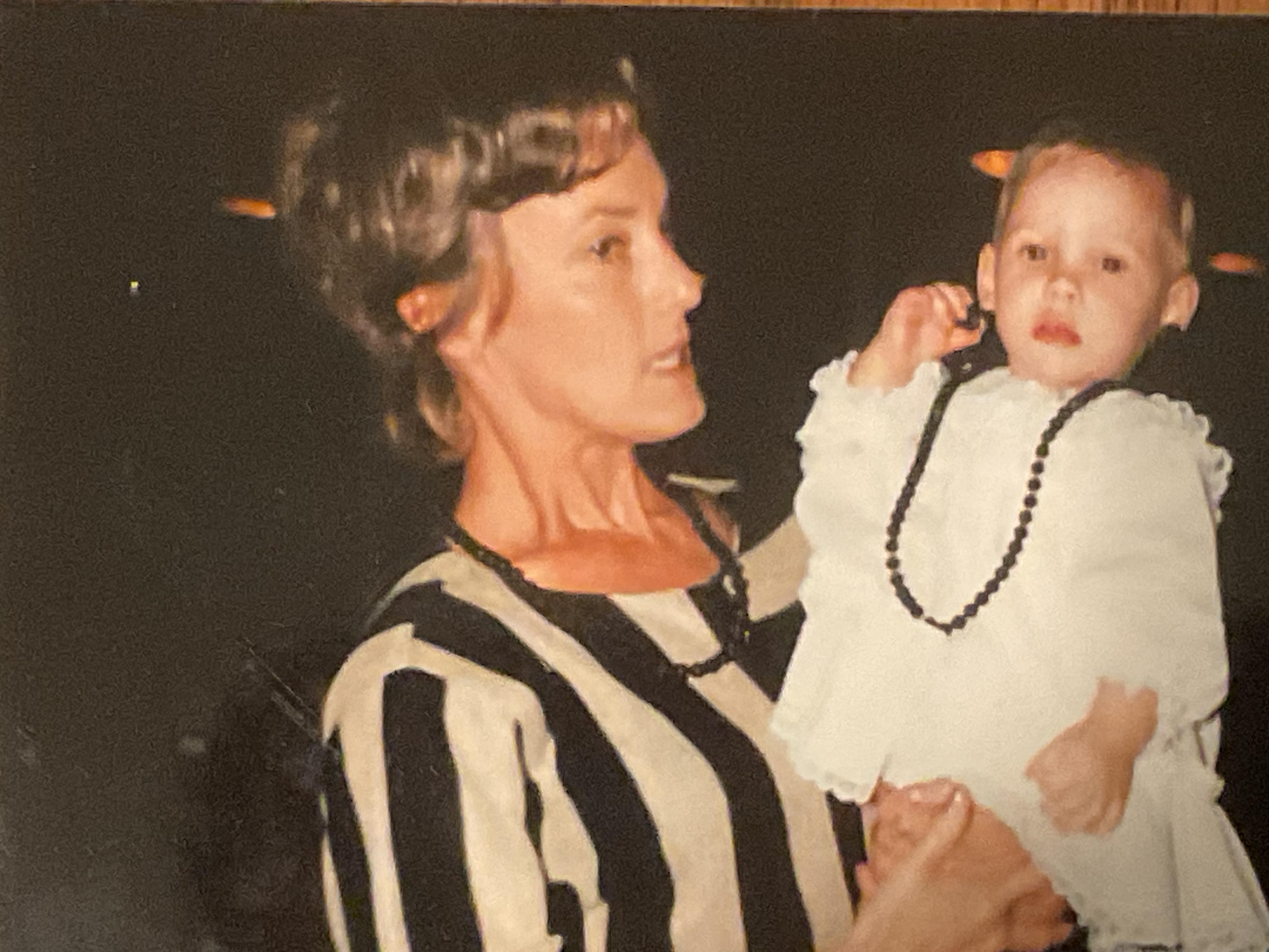 A woman dressed in a striped outfit lovingly holds a baby in a light dress during a gathering.