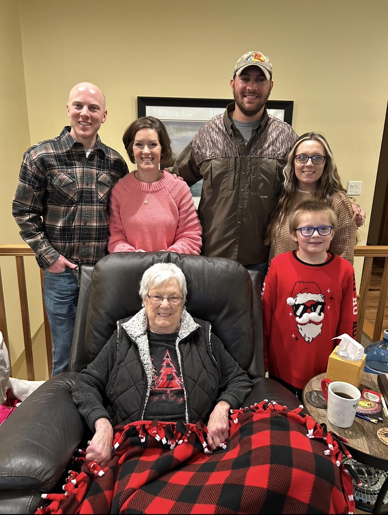 Family members pose happily with grandmother in a warm living room during winter festivities.