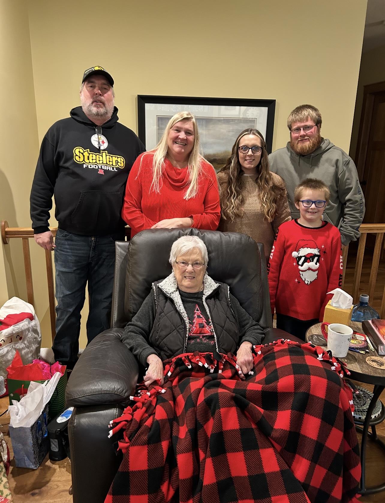 A family enjoys a joyful holiday moment with their grandmother by the fireplace.
