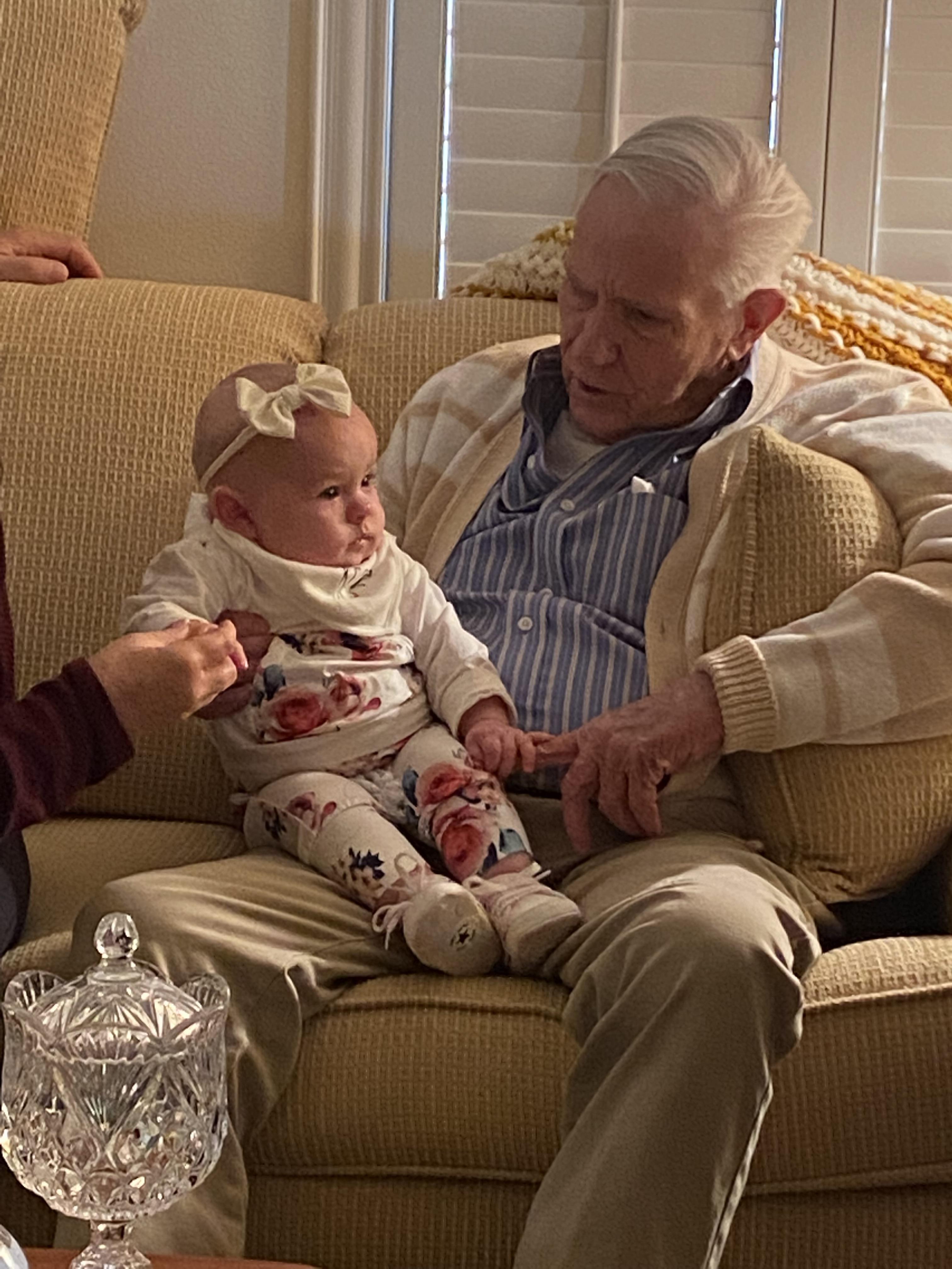 Grandfather and baby girl share a tender moment together while sitting on a sofa in a warm home.