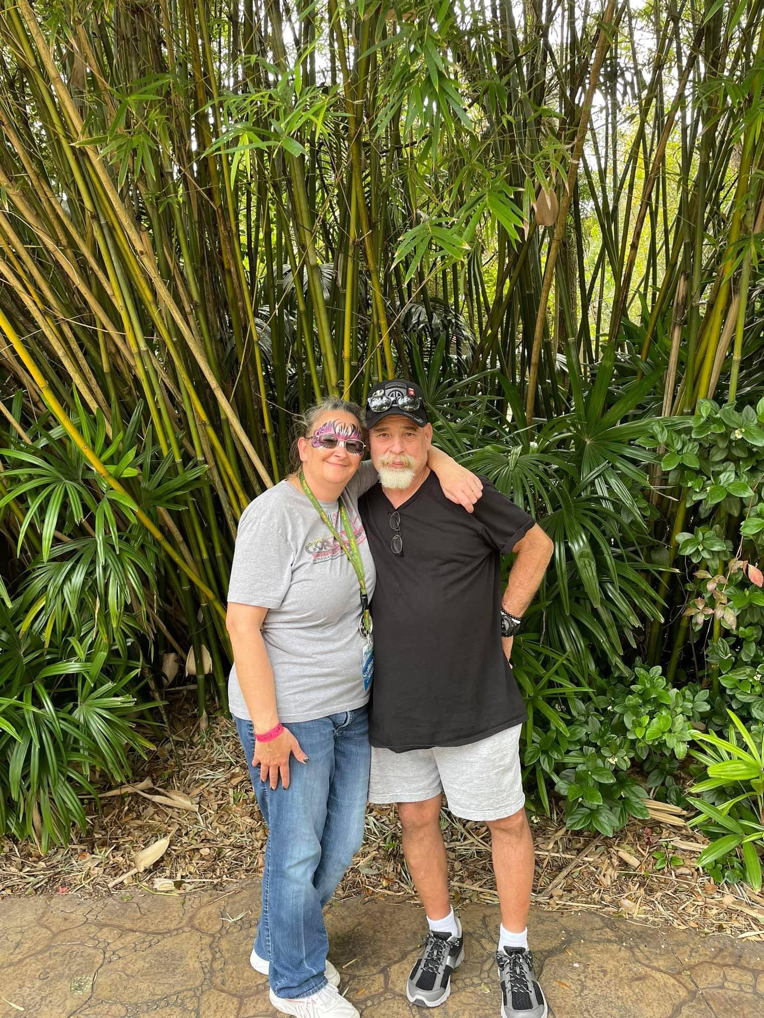 Two people smile and embrace amidst vibrant greenery in a tropical garden.