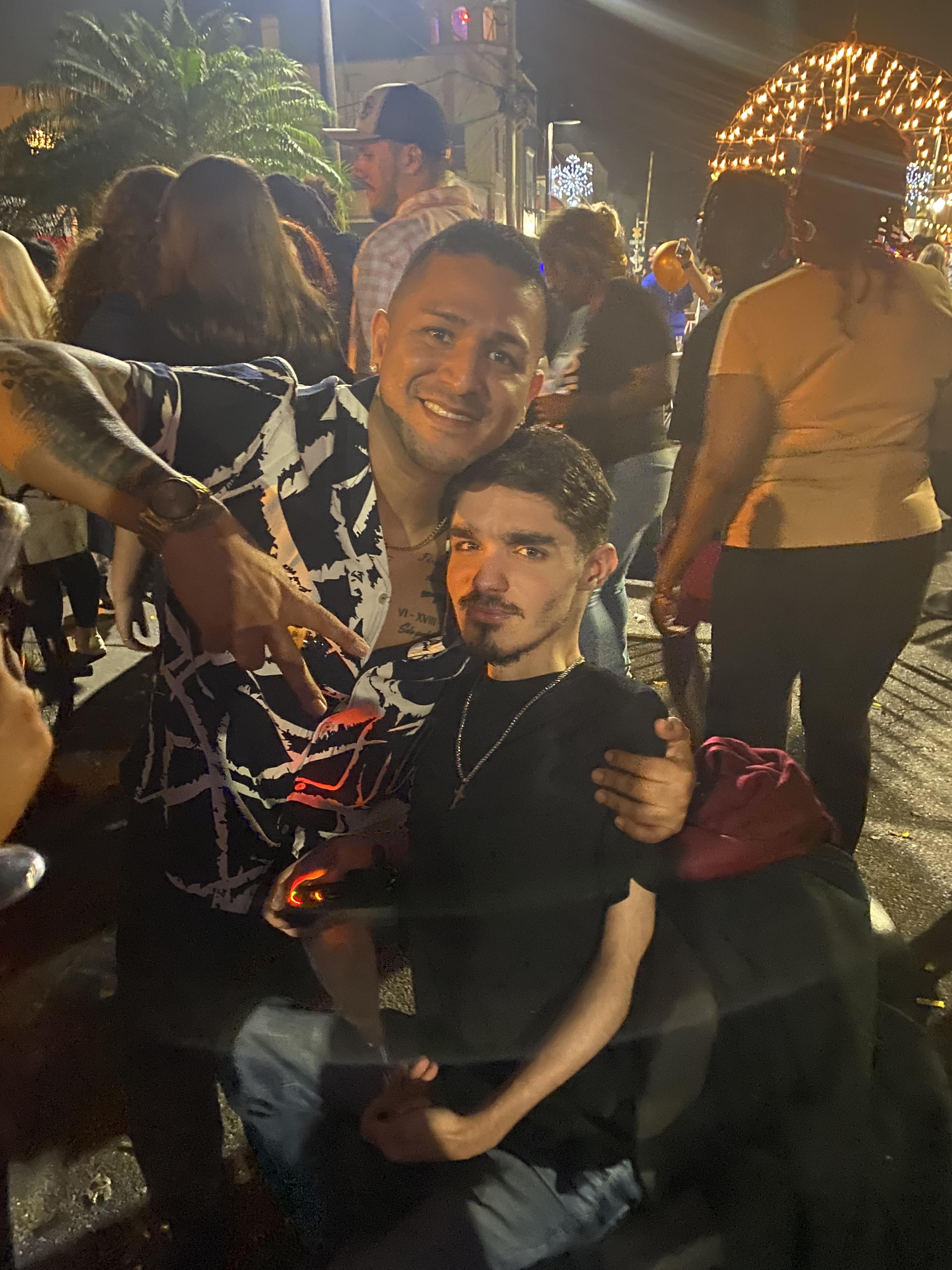 Two friends pose happily together at a bustling street celebration filled with lights.