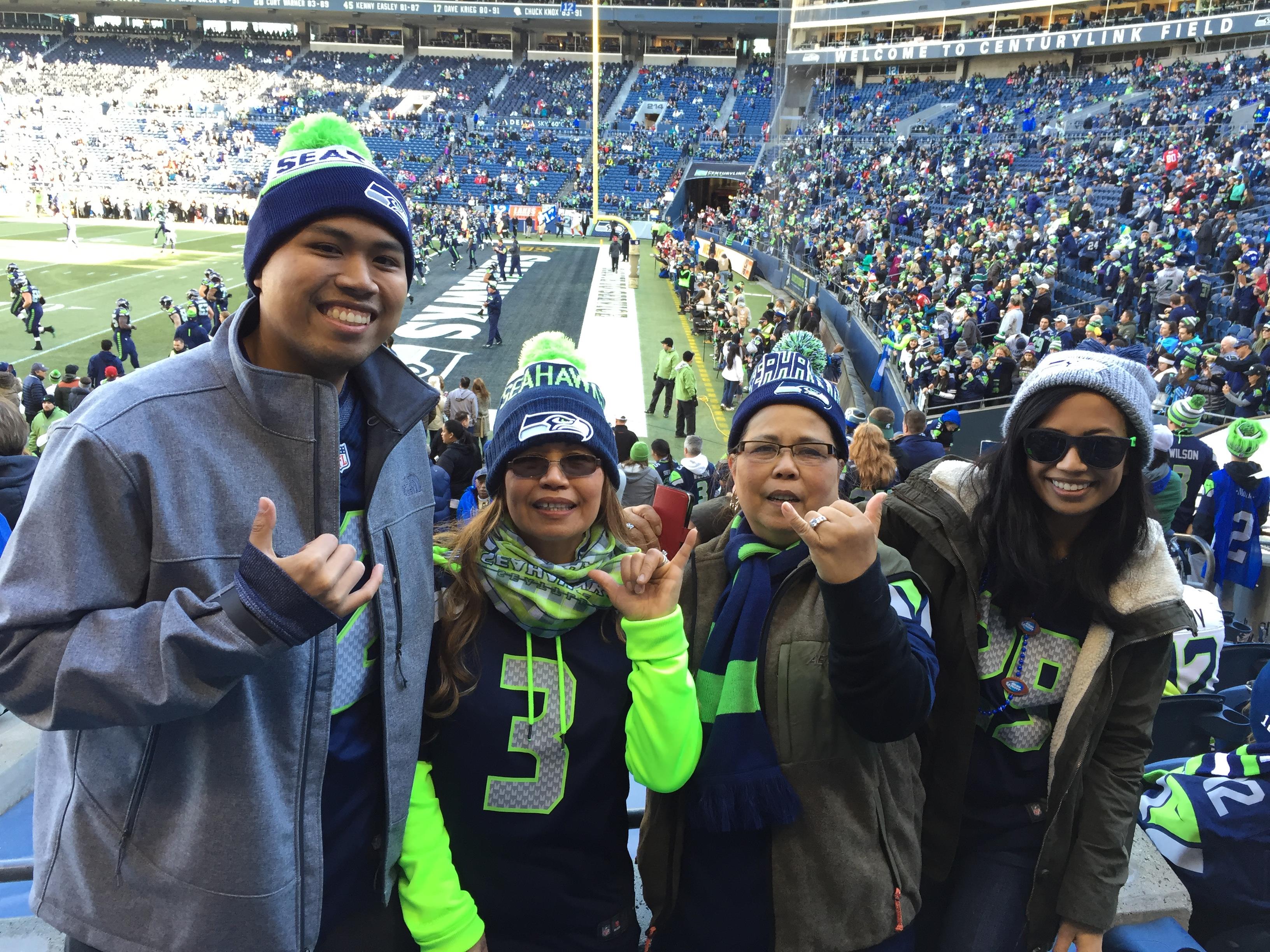 Four fans in team apparel pose joyfully, celebrating their team at the crowded game.